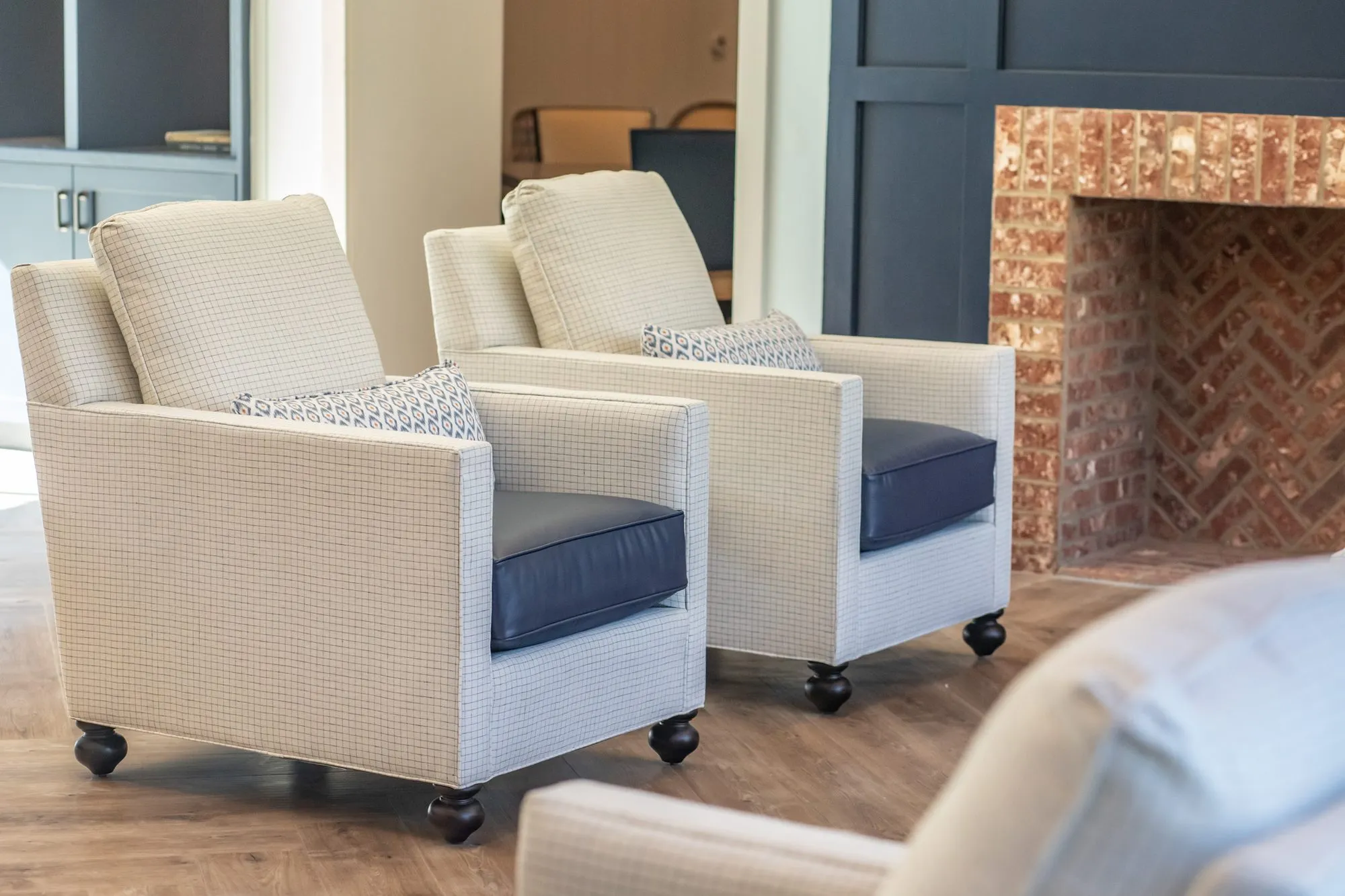 Senior living interior detail: two cream check armchairs with navy seats beside the herringbone brick firebox