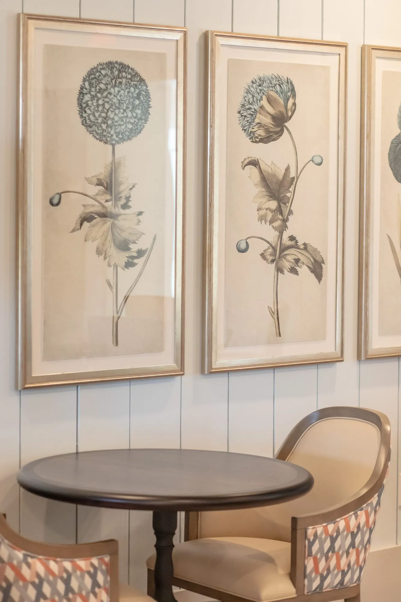 Senior living interior detail: framed botanical prints of an allium and a poppy above a round dark table