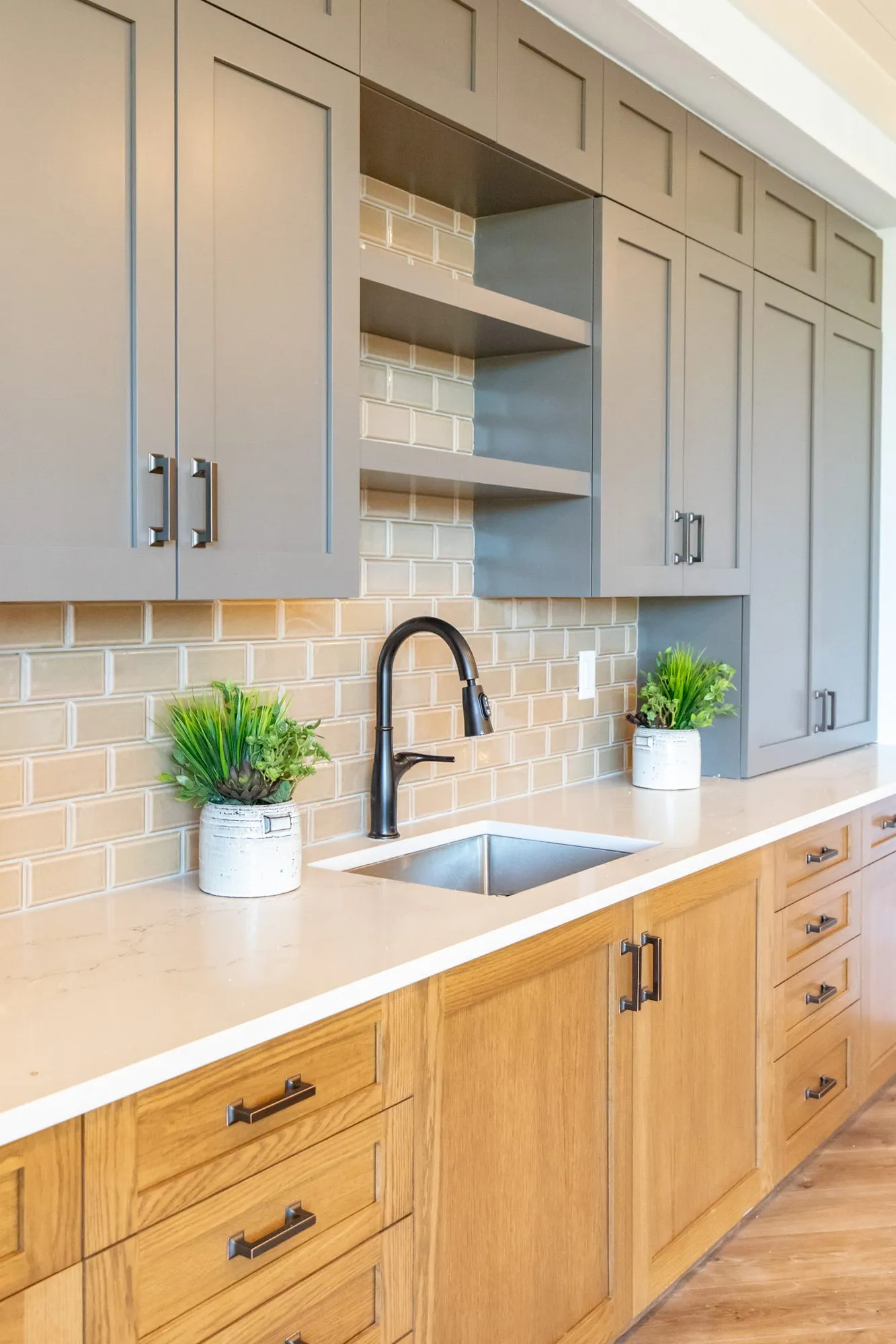 Senior living kitchenette at an angle, plants by a black faucet, grey uppers and oak drawers