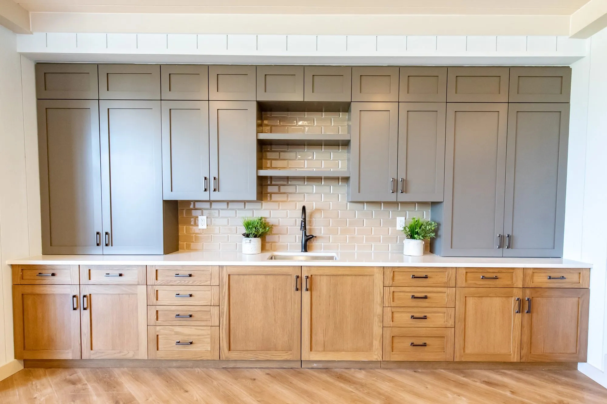Senior living kitchenette wall with grey upper cabinets, open shelves over tan subway tile and oak base cabinets