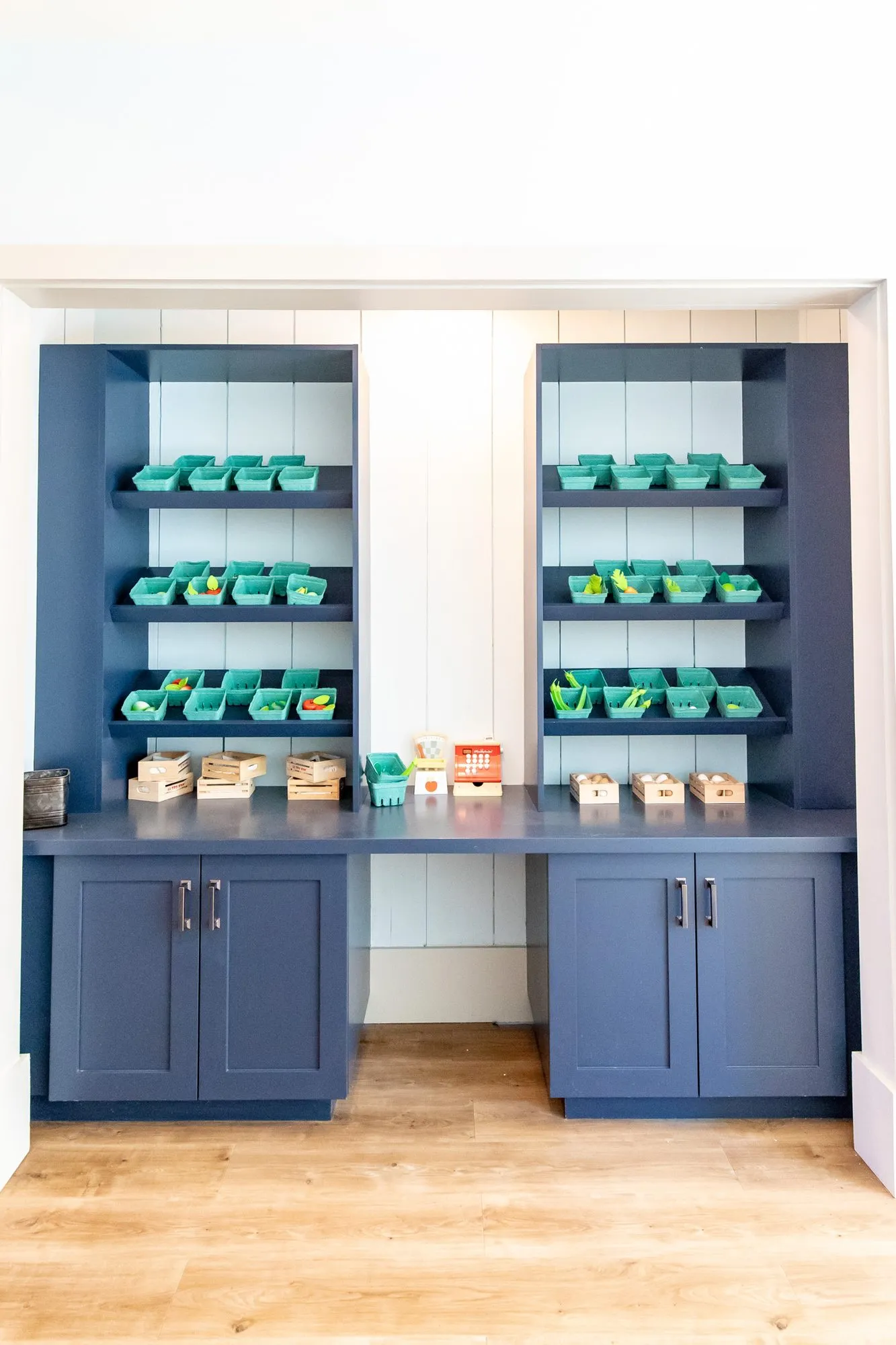 Senior living market display of two navy shelving units with green berry baskets of play produce above cabinets
