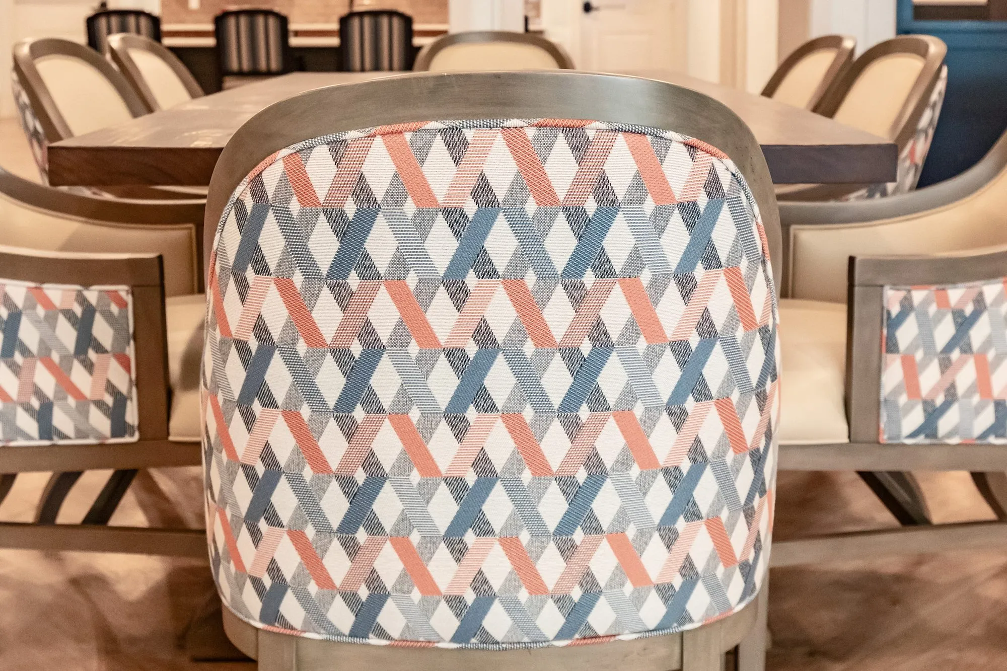 Senior living interior detail: geometric coral and blue chair back at a dining table, more chairs around it