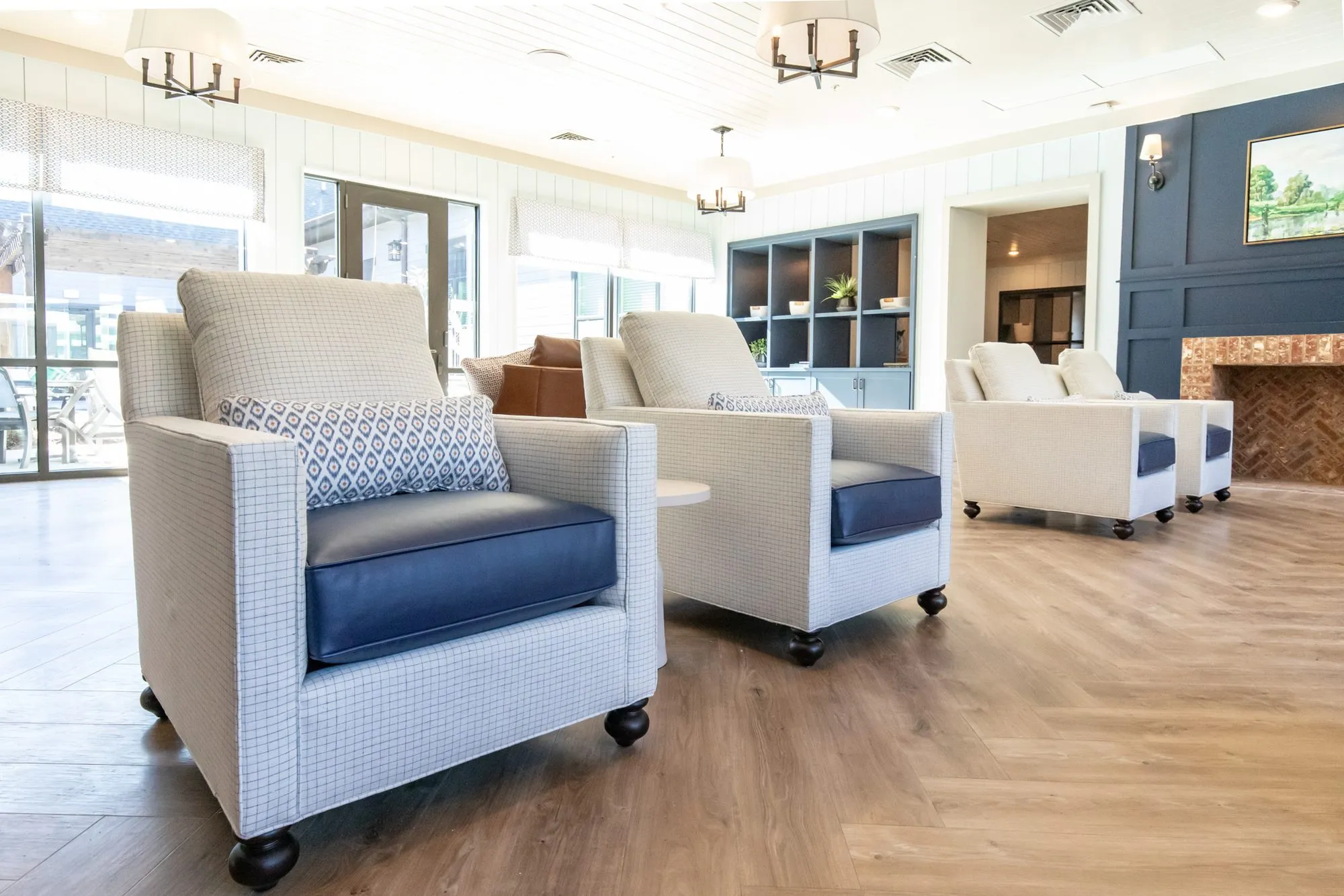 Senior living lounge with cream check armchairs with navy seats on casters toward a navy wall and brick fireplace