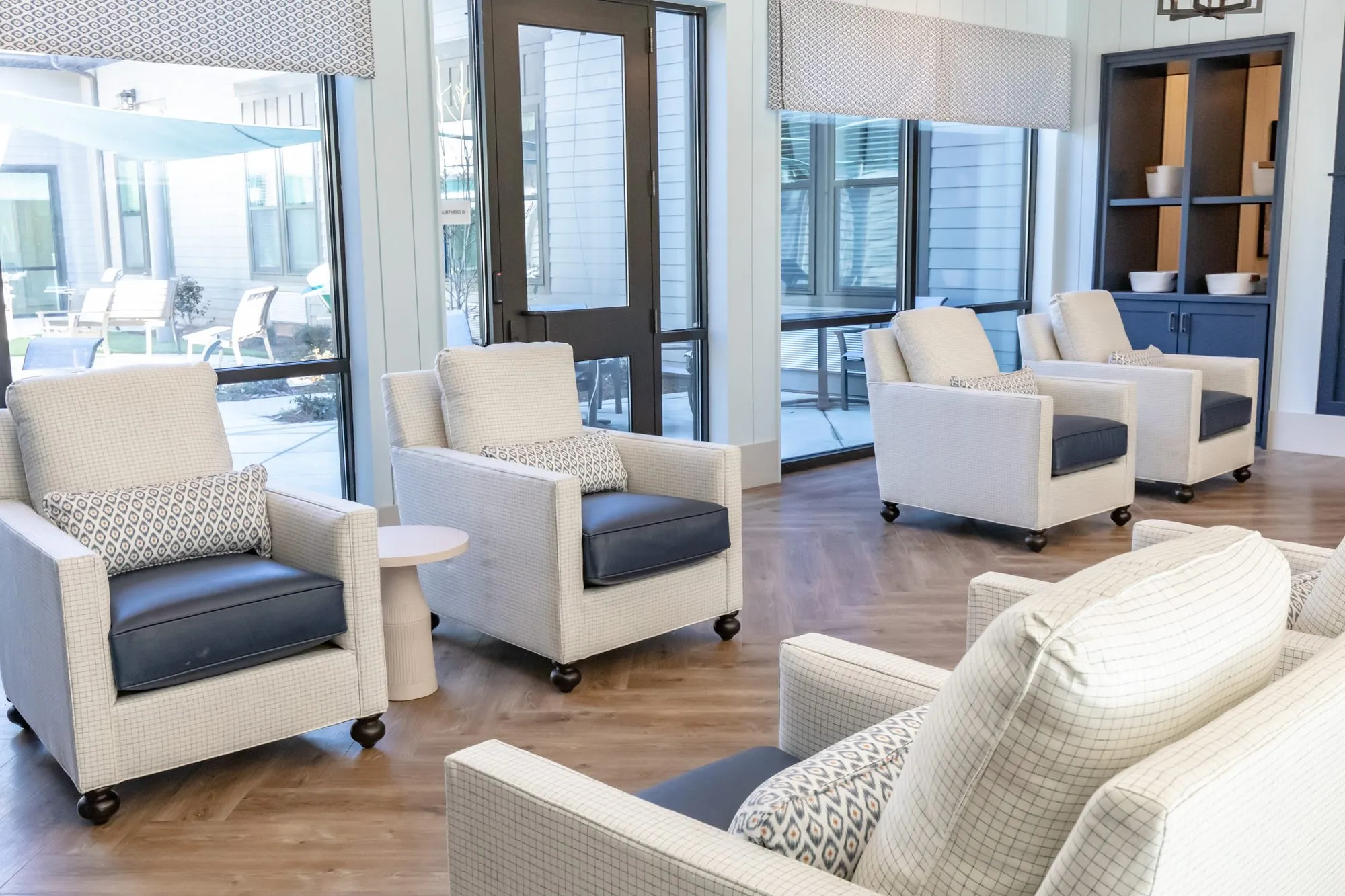 Senior living lounge with cream check armchairs with navy seats by tall windows and a door to the patio