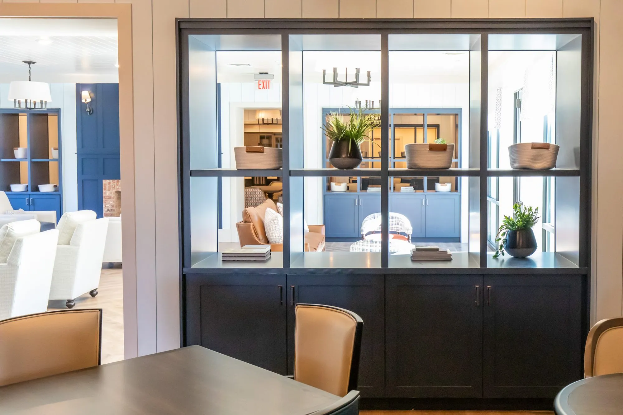 Senior living interior detail: navy cabinet with a glazed display of baskets and plants between two rooms, a dining table