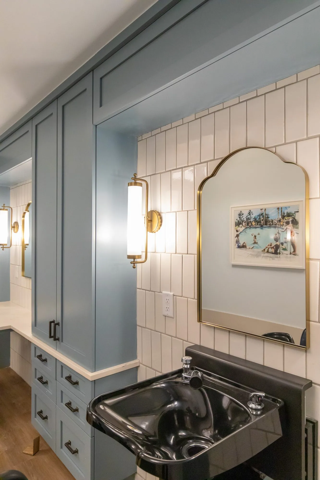 Senior living salon detail: black shampoo bowl below an arched brass mirror and glass sconce on white tile