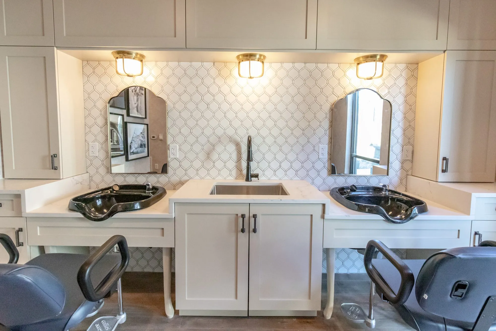 Senior living salon wash station with two black shampoo bowls flanking a sink, arched mirrors and brass ceiling lights