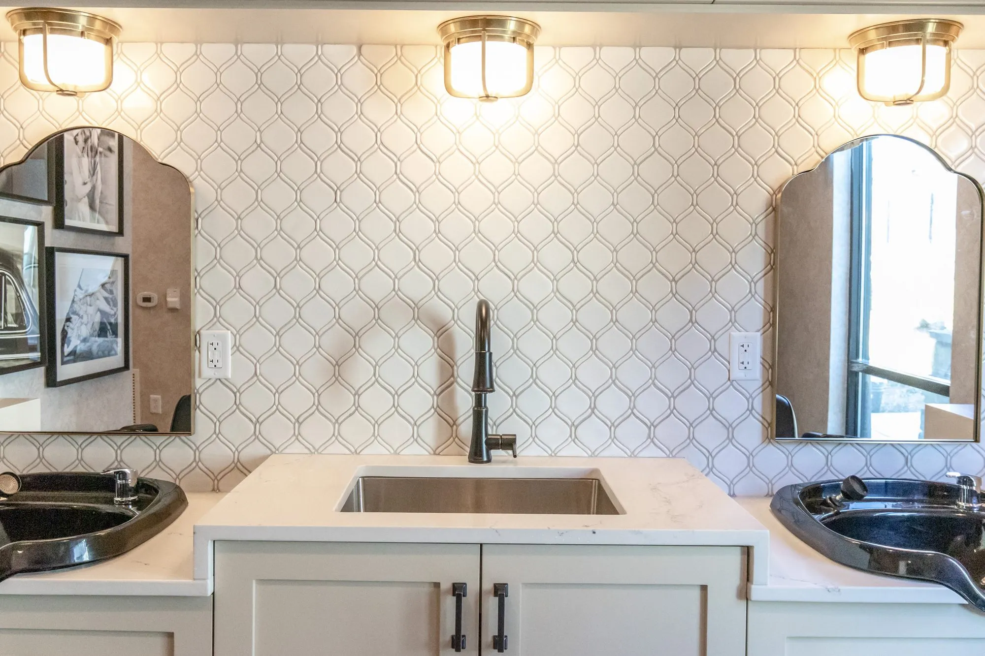Senior living salon sink between black shampoo bowls under brass flush lights on white ogee tile