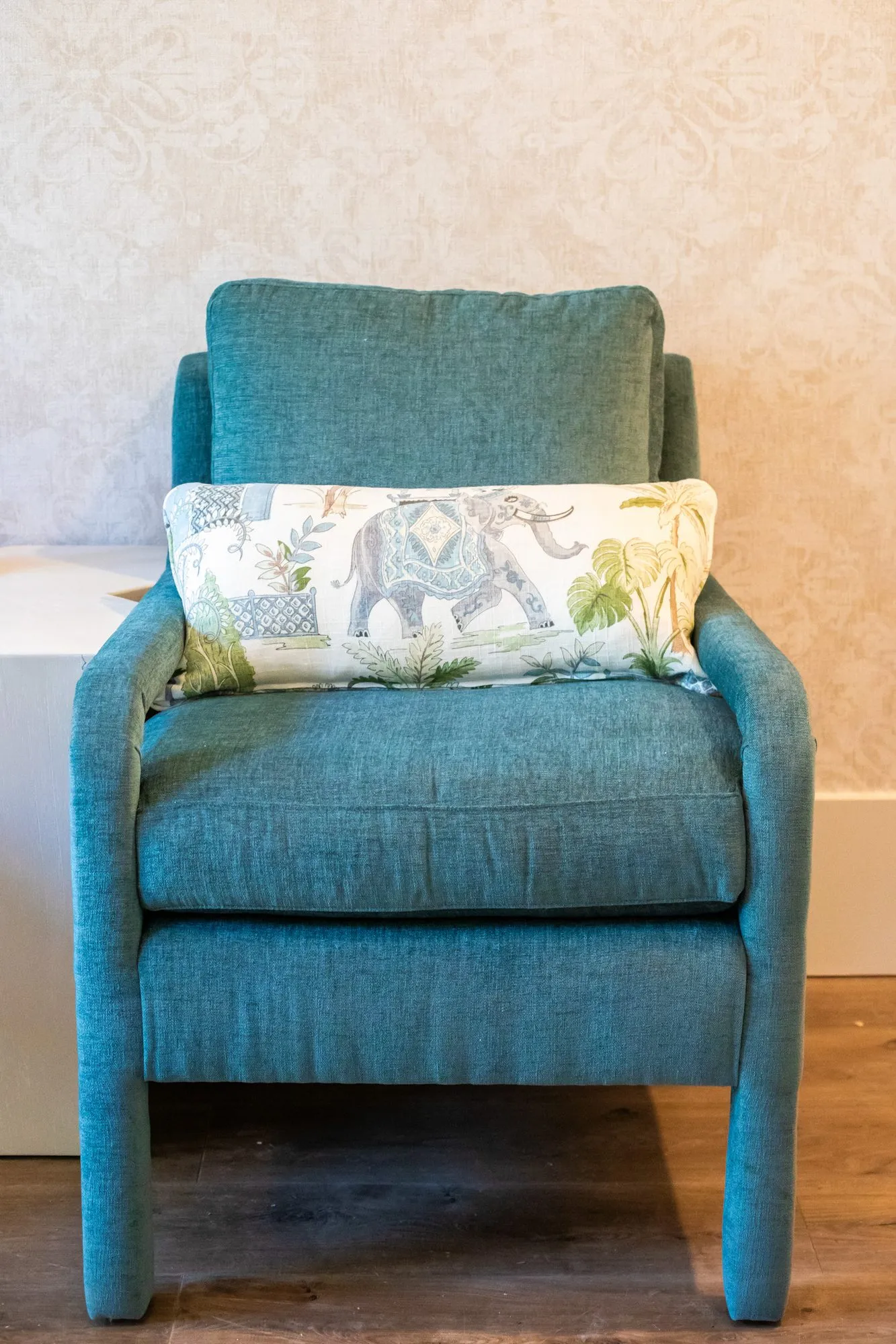 Senior living interior detail: teal upholstered armchair with an elephant print lumbar pillow