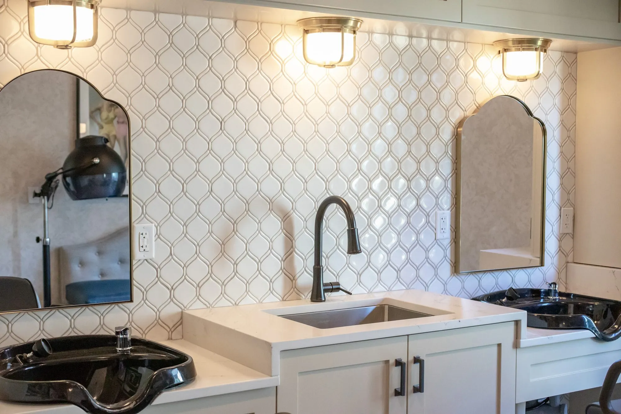 Senior living salon wash station at an angle, black shampoo bowls, a hood dryer reflected in an arched mirror