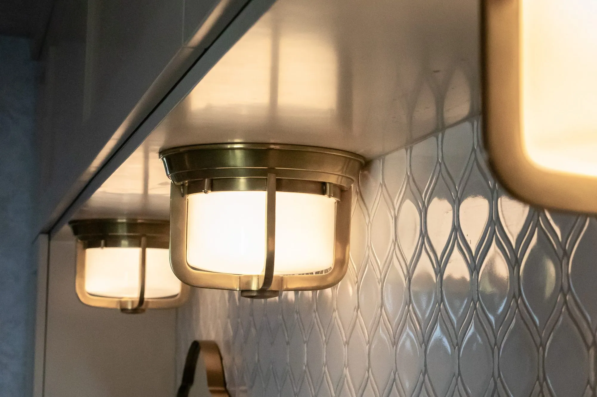 Senior living interior detail: brass flush ceiling lights under a soffit against glossy white ogee tile