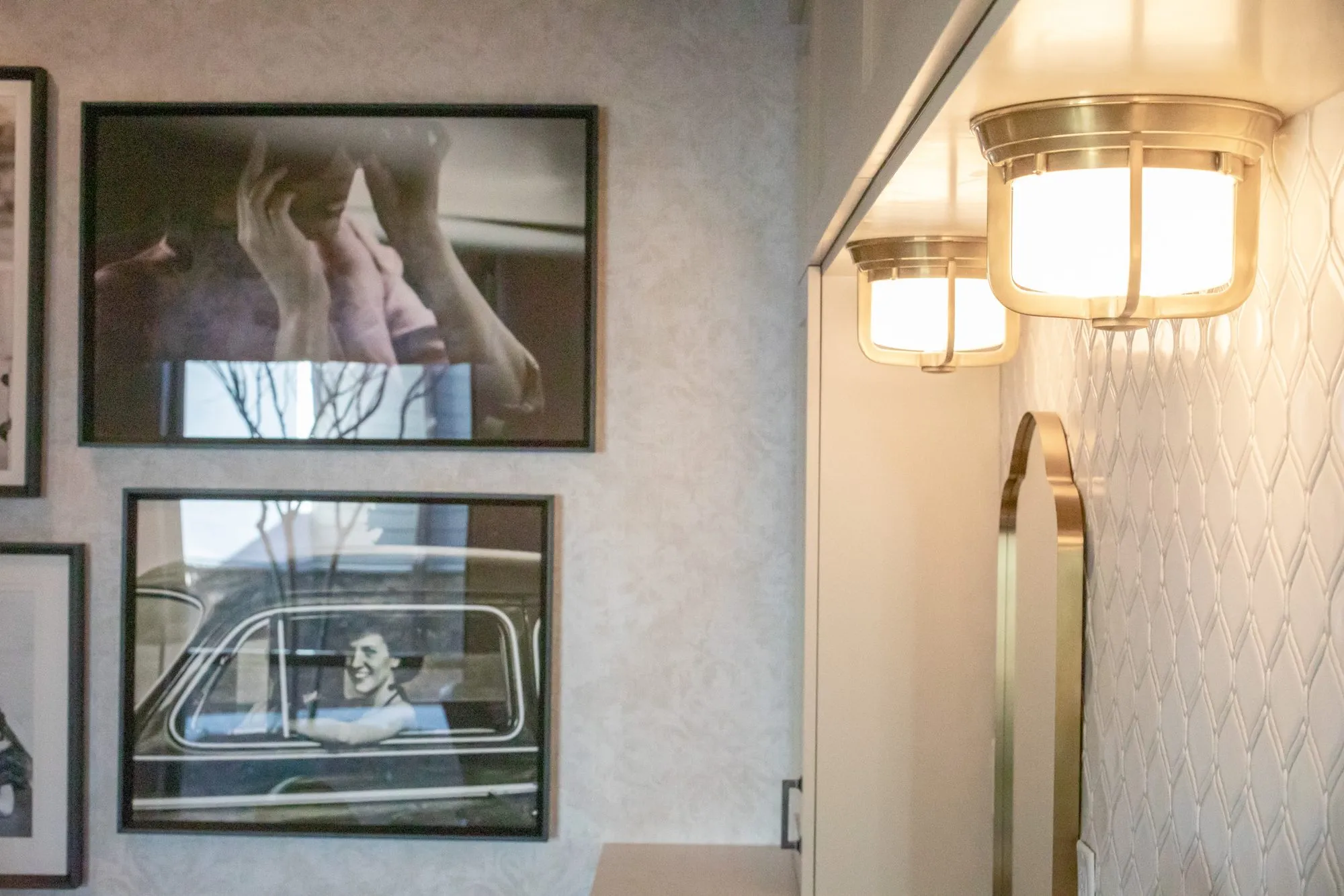 Senior living interior detail: black and white photographs on damask wallcovering beside brass lights and ogee tile