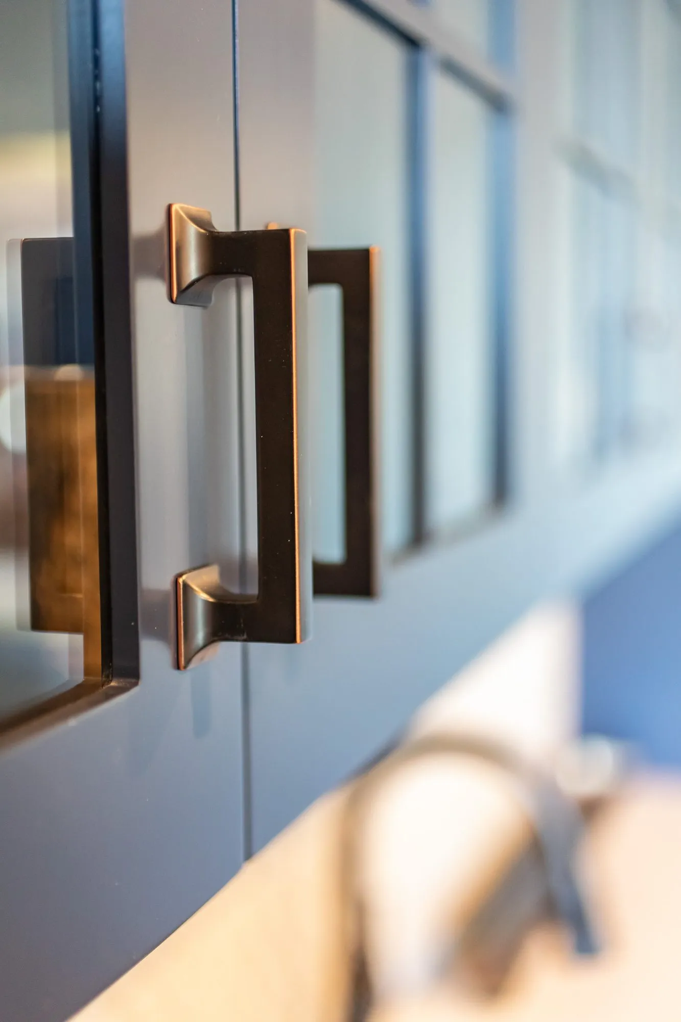 Senior living interior detail: bronze pull on navy glass front cabinet doors