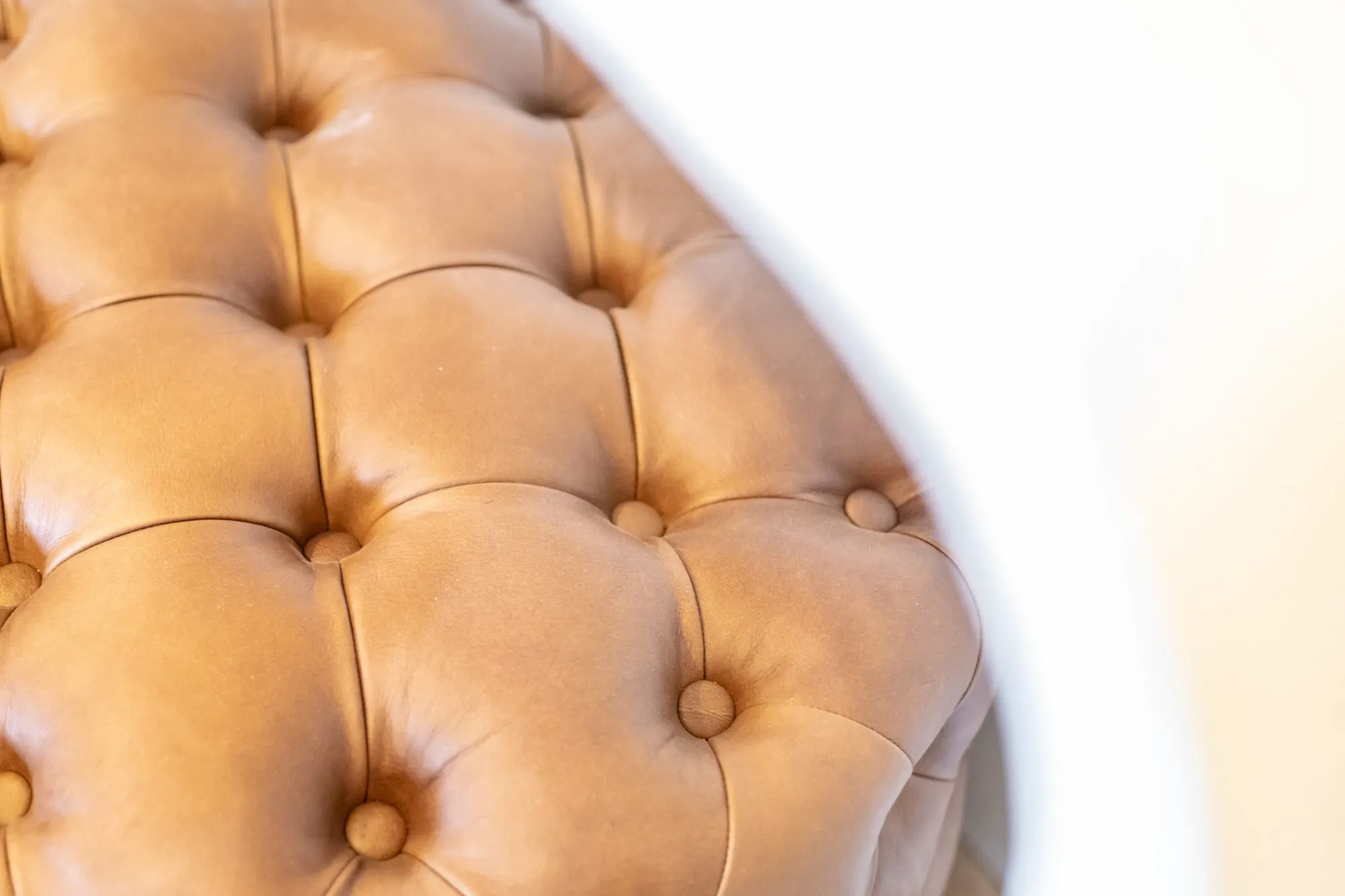 Senior living interior detail: cognac leather tufted ottoman with buttons