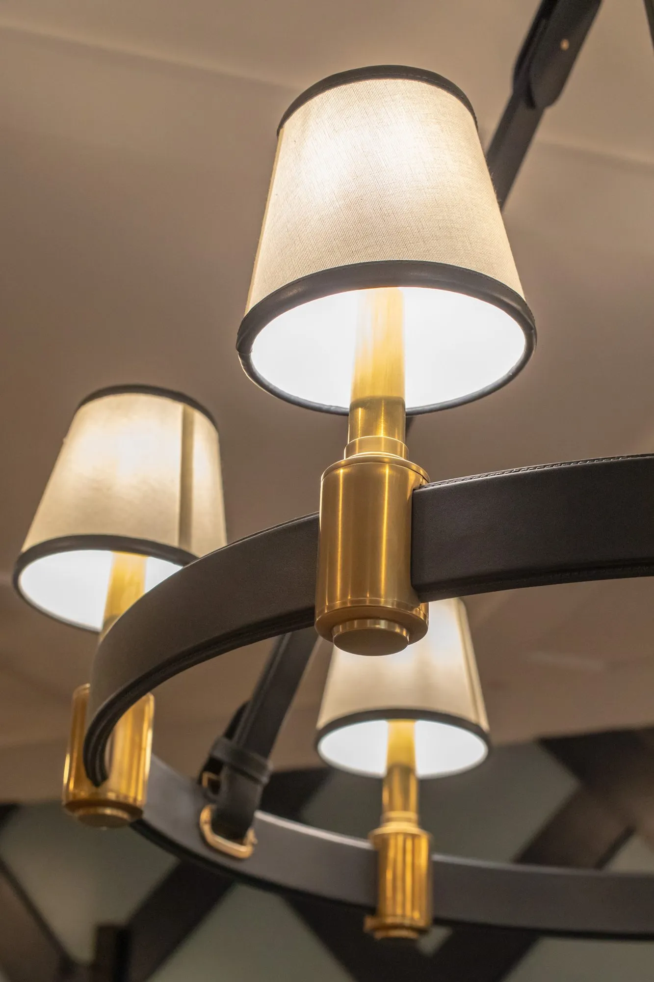 Senior living interior detail: looking up at a black ring chandelier with brass fittings and white shades