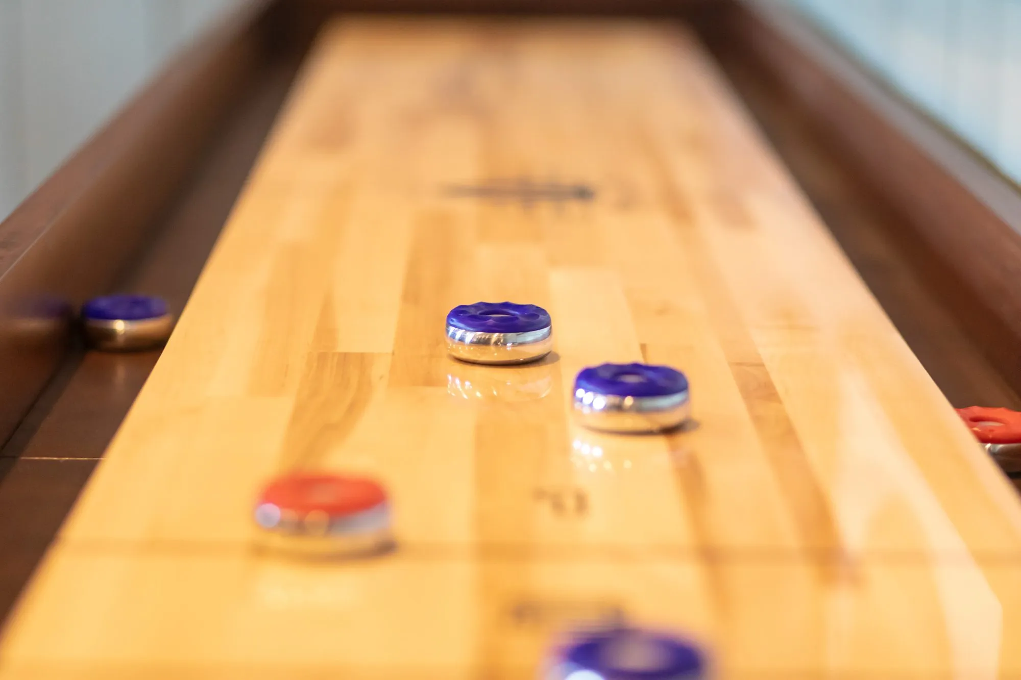 Senior living interior detail: shuffleboard table with blue and red pucks on the polished maple surface