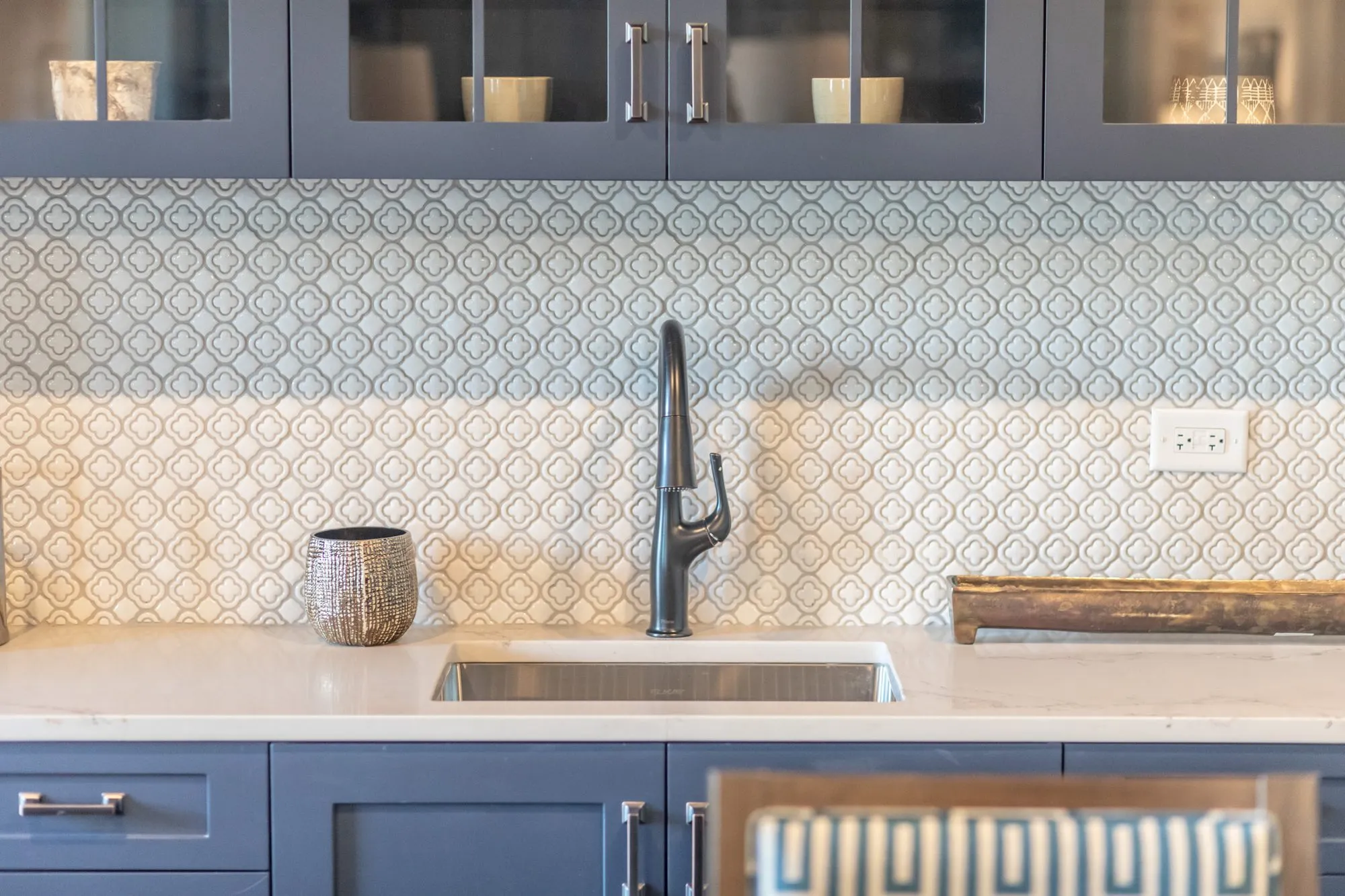 Senior living kitchenette with navy cabinets, glass front uppers, a geometric tile backsplash and a black faucet