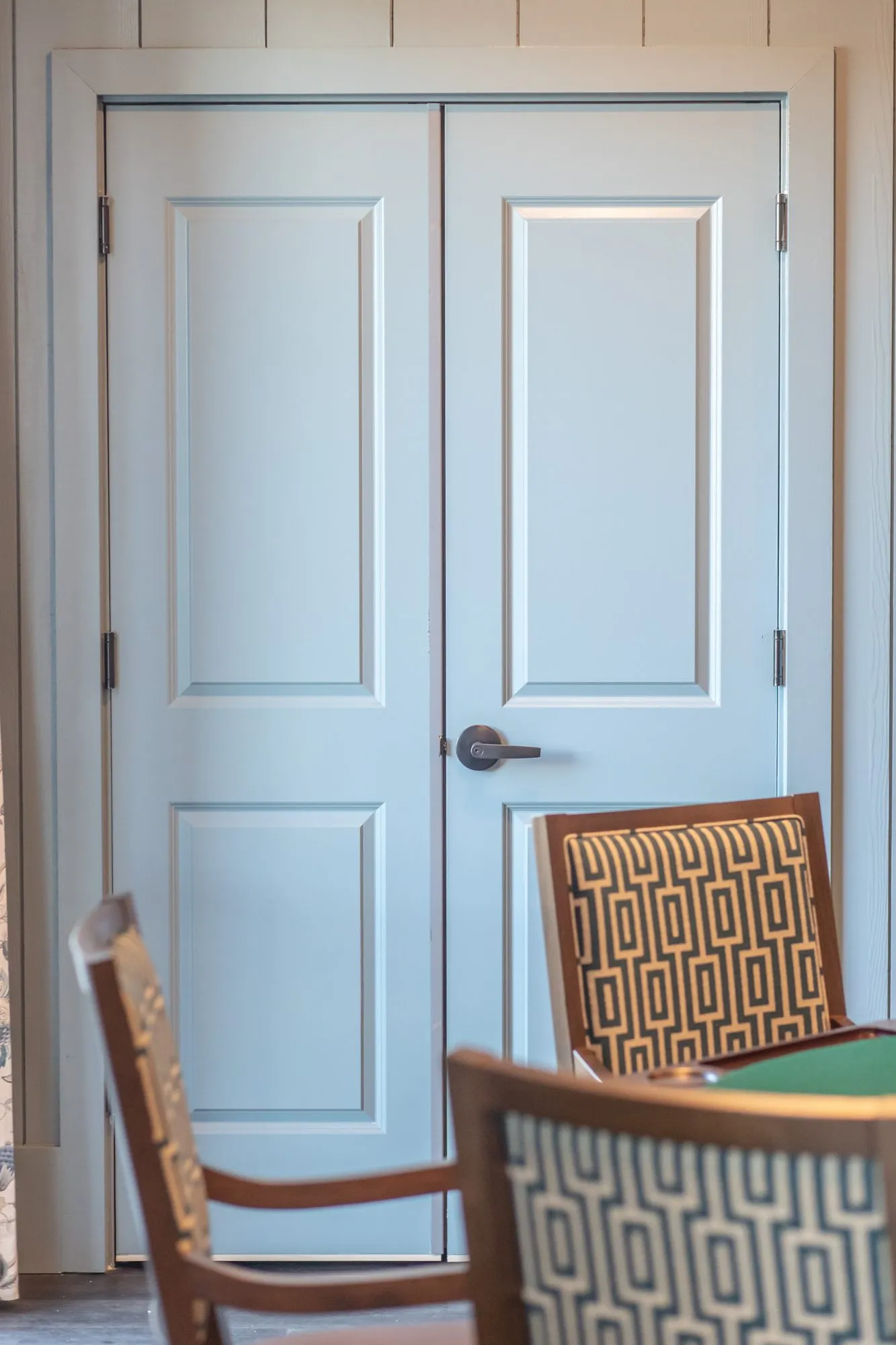 Senior living card room with white double doors behind a card table and geometric back chairs