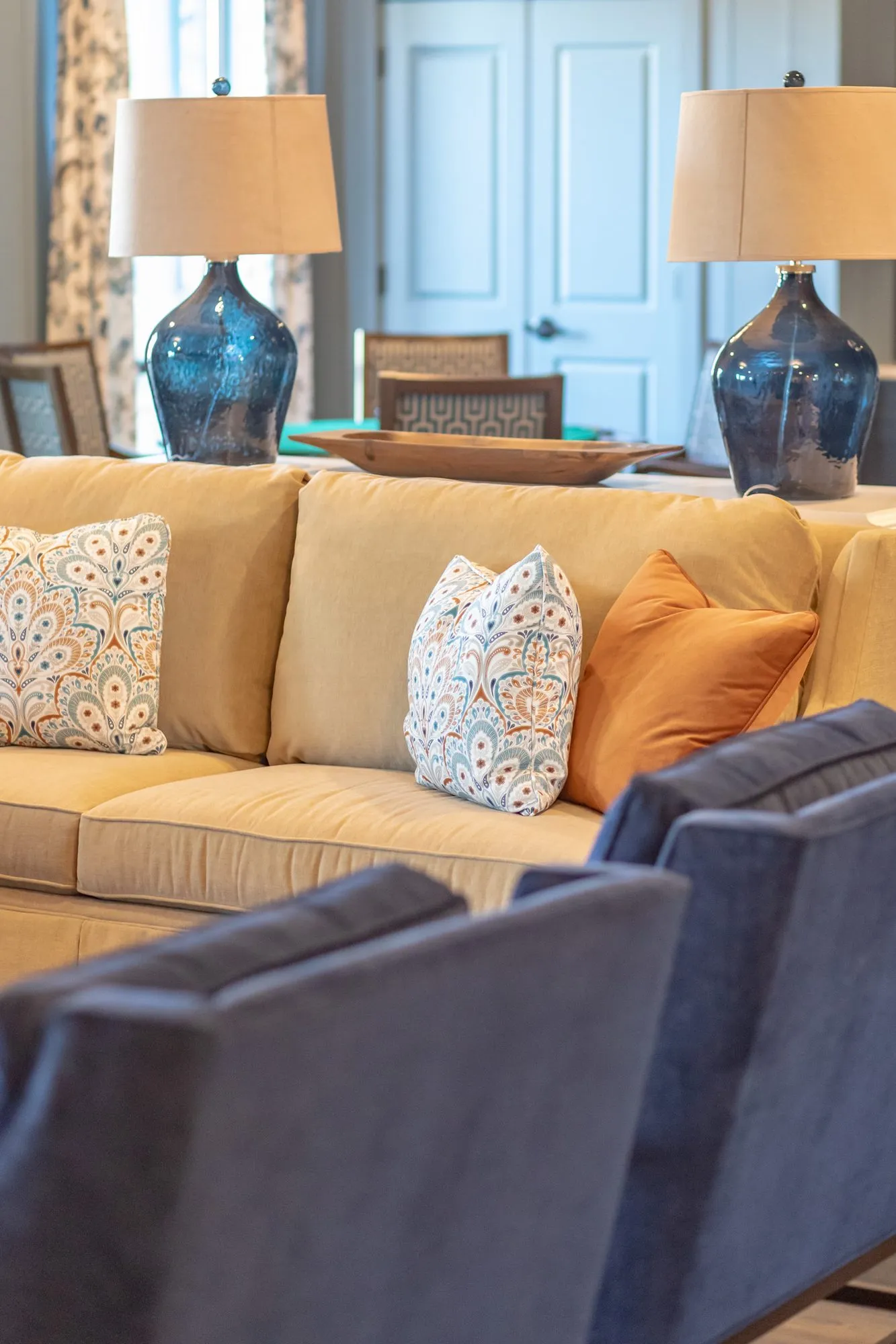 Senior living lounge seen over navy armchairs to a camel sofa with patterned pillows and two navy glass lamps