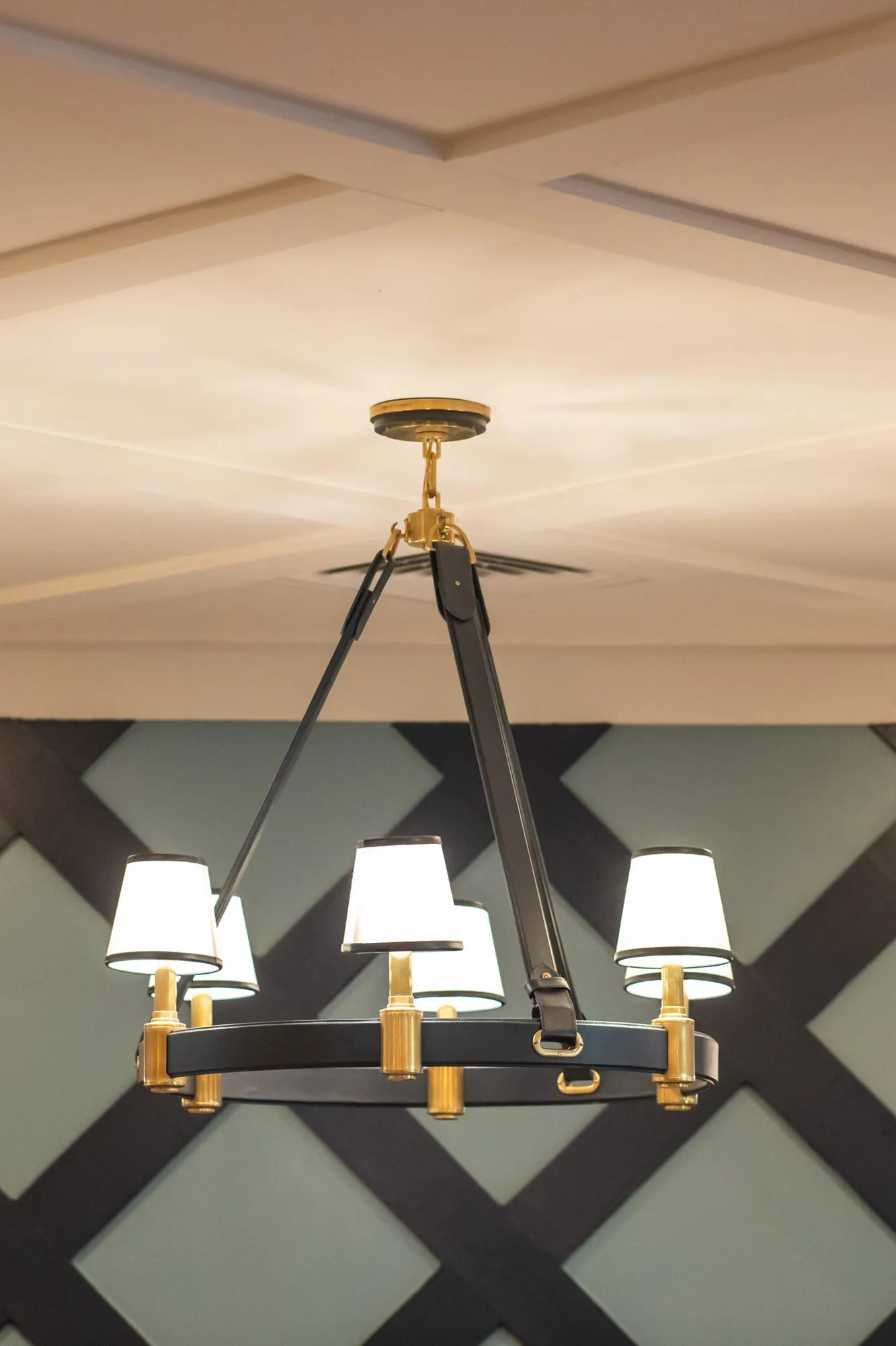 Senior living interior detail: black and brass ring chandelier with white shades before a navy lattice wall