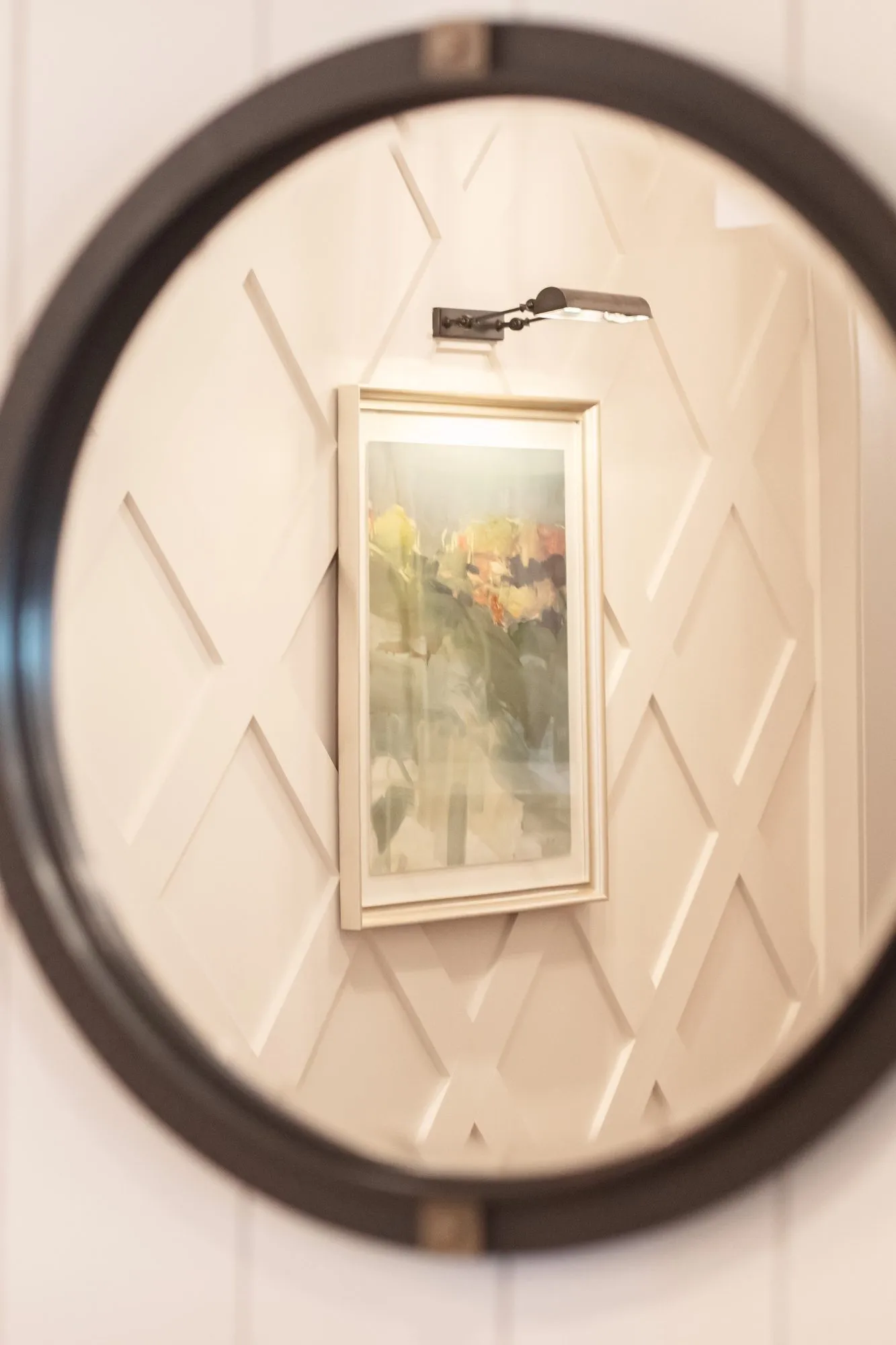 Senior living interior detail: round black mirror reflecting a framed painting on diamond panelled millwork