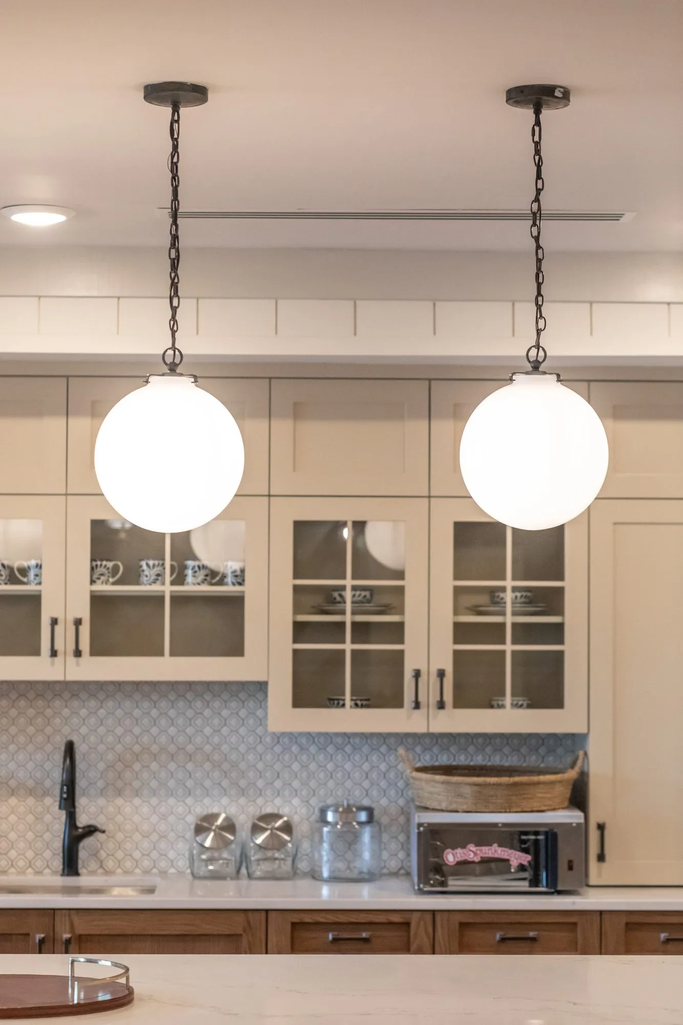 Senior living kitchenette with two white globe pendants before cream glass front cabinets