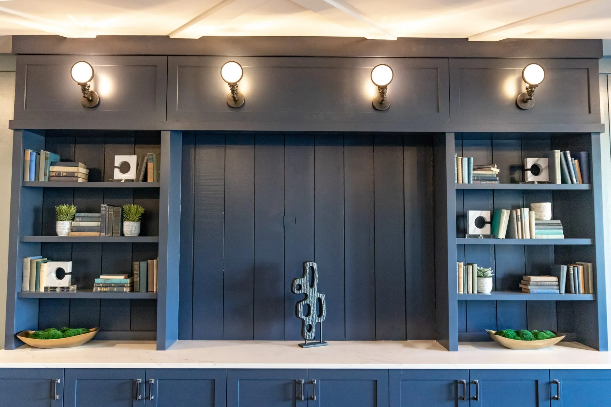 Senior living interior detail: navy built-in bookcases flanking a plank panel with a sculpture, brass sconces above