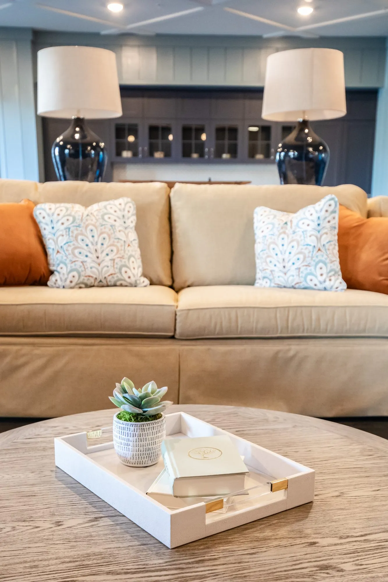 Senior living interior detail: camel sofa with paisley and orange pillows behind a round wood coffee table