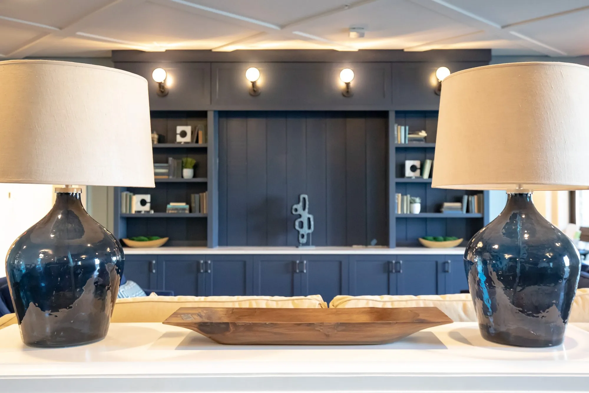 Senior living interior detail: navy glass lamps on a white console framing the navy built-in bookcases beyond