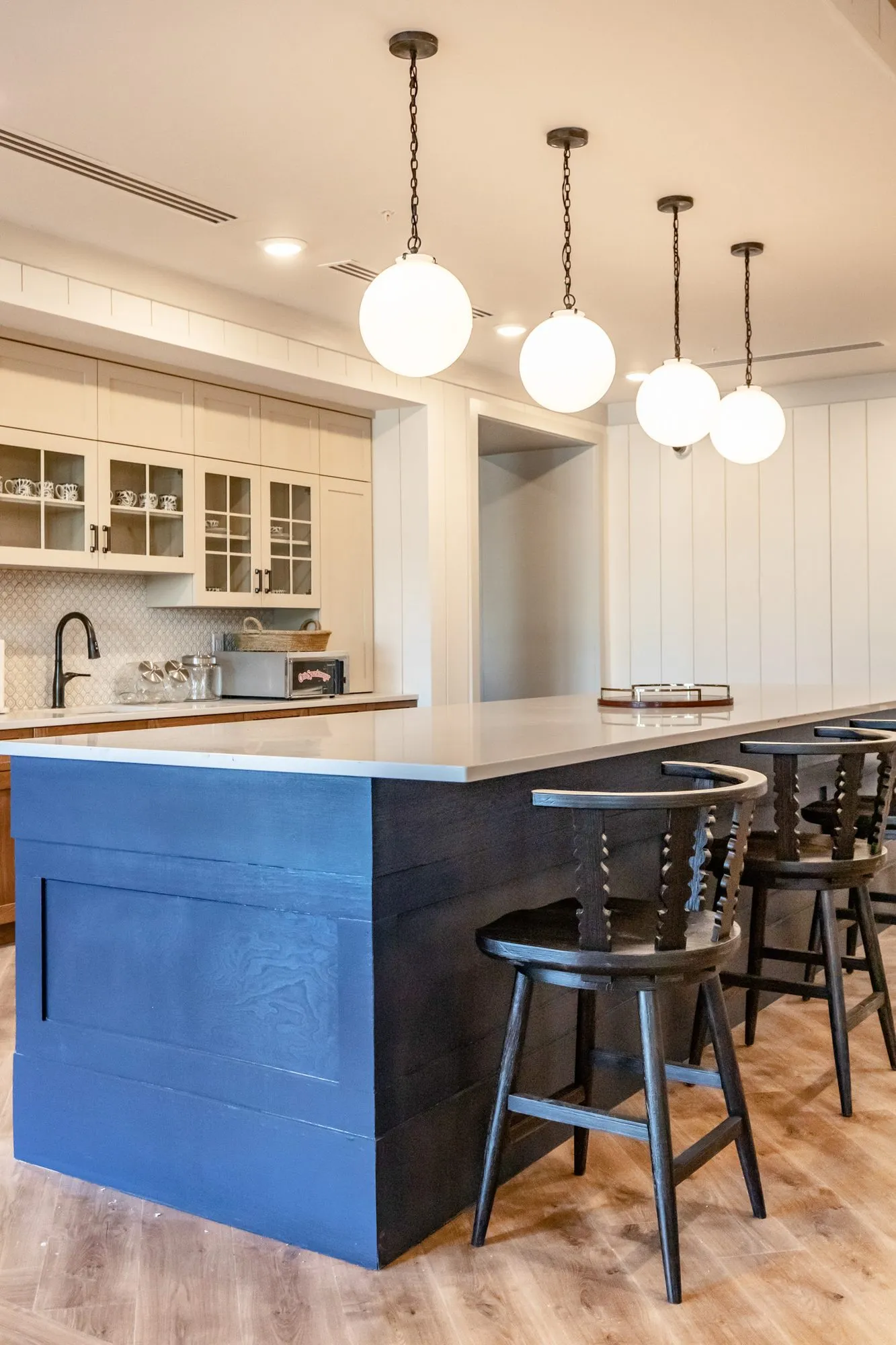 Senior living kitchen with a navy plank island and spindle back barstools below white globe pendants