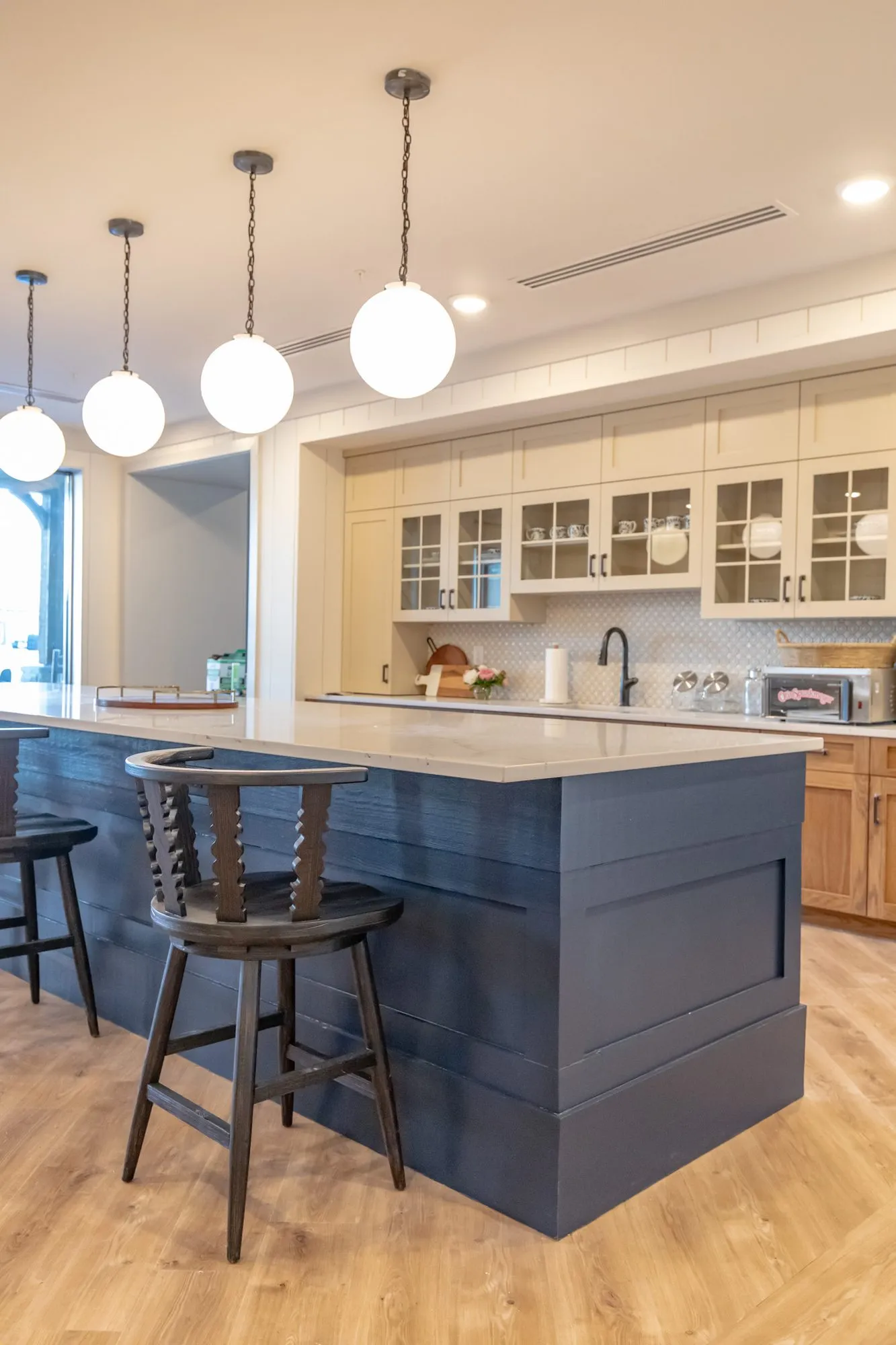 Senior living kitchen at the end of the navy island, barstools and globe pendants before cream cabinets