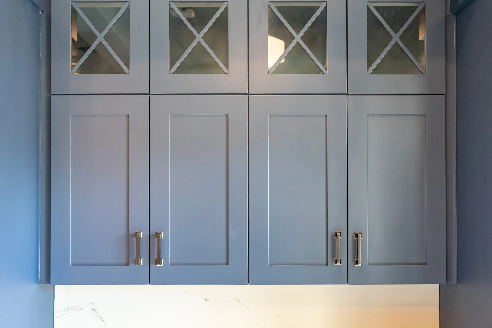 Senior living interior detail: grey blue cabinets with X mullion glass doors above a marble counter