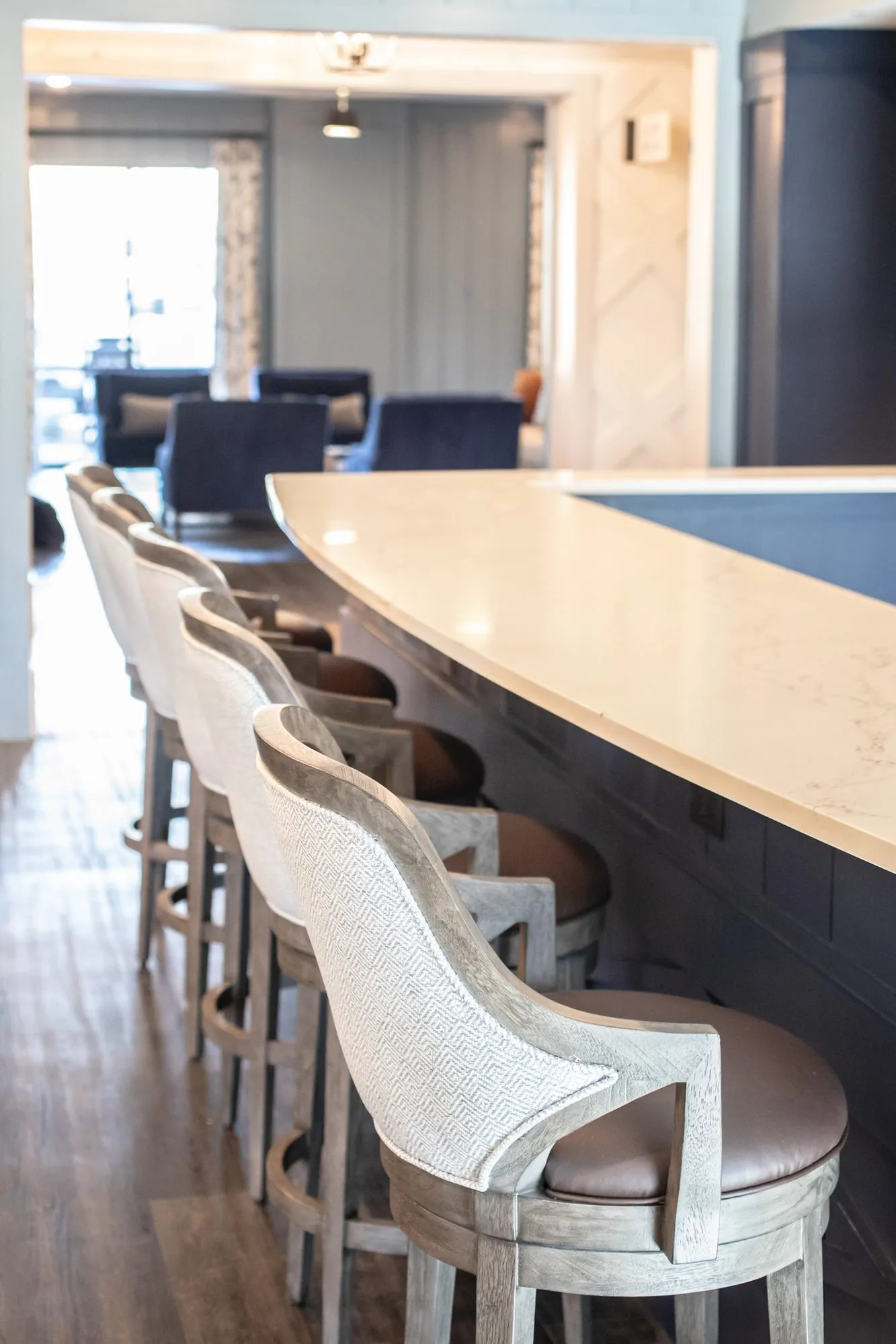 Senior living bar with woven back swivel barstools lining a white counter, a lounge beyond