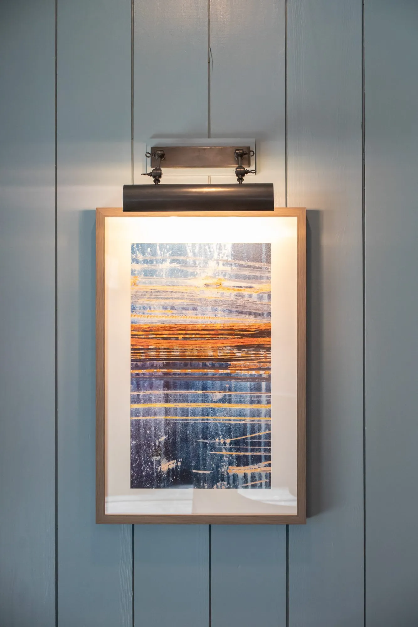 Senior living interior detail: framed blue and orange abstract with a picture light on blue paneling