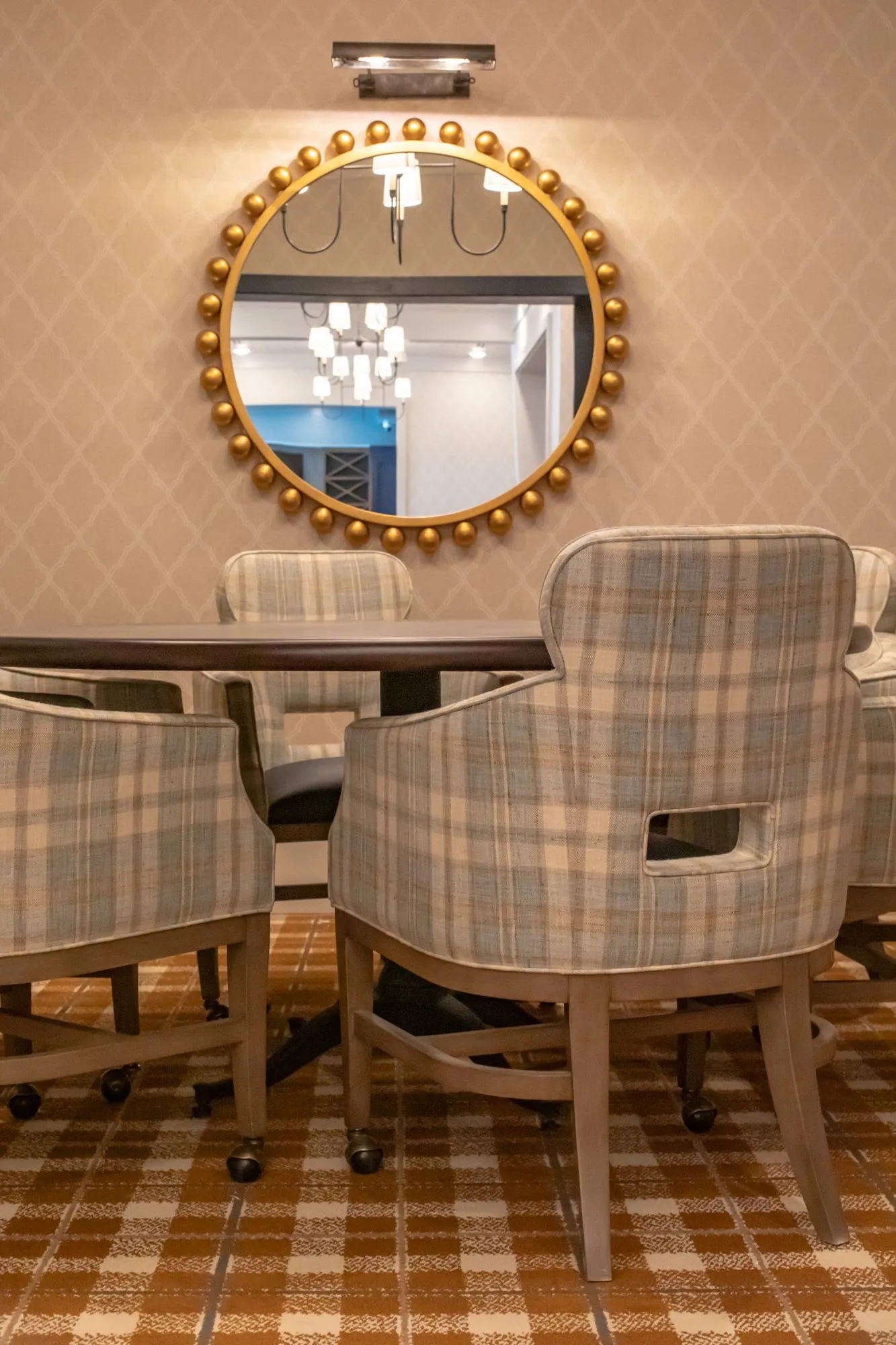 Senior living private dining room with plaid chairs at a round table below a gilt beaded mirror