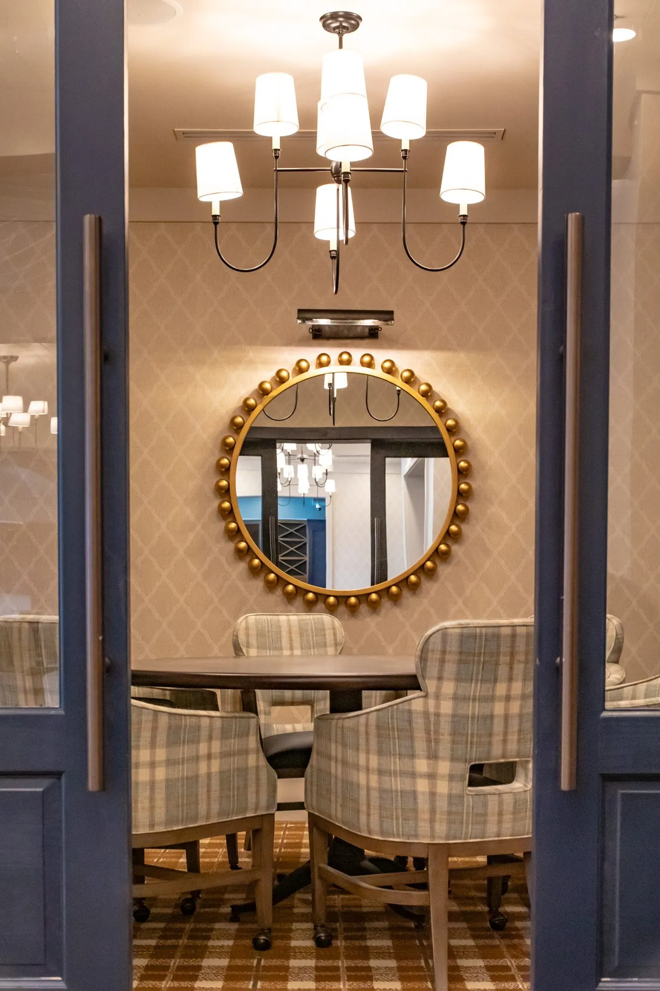 Senior living private dining room through navy double doors, a gilt beaded mirror and chandelier over a round table