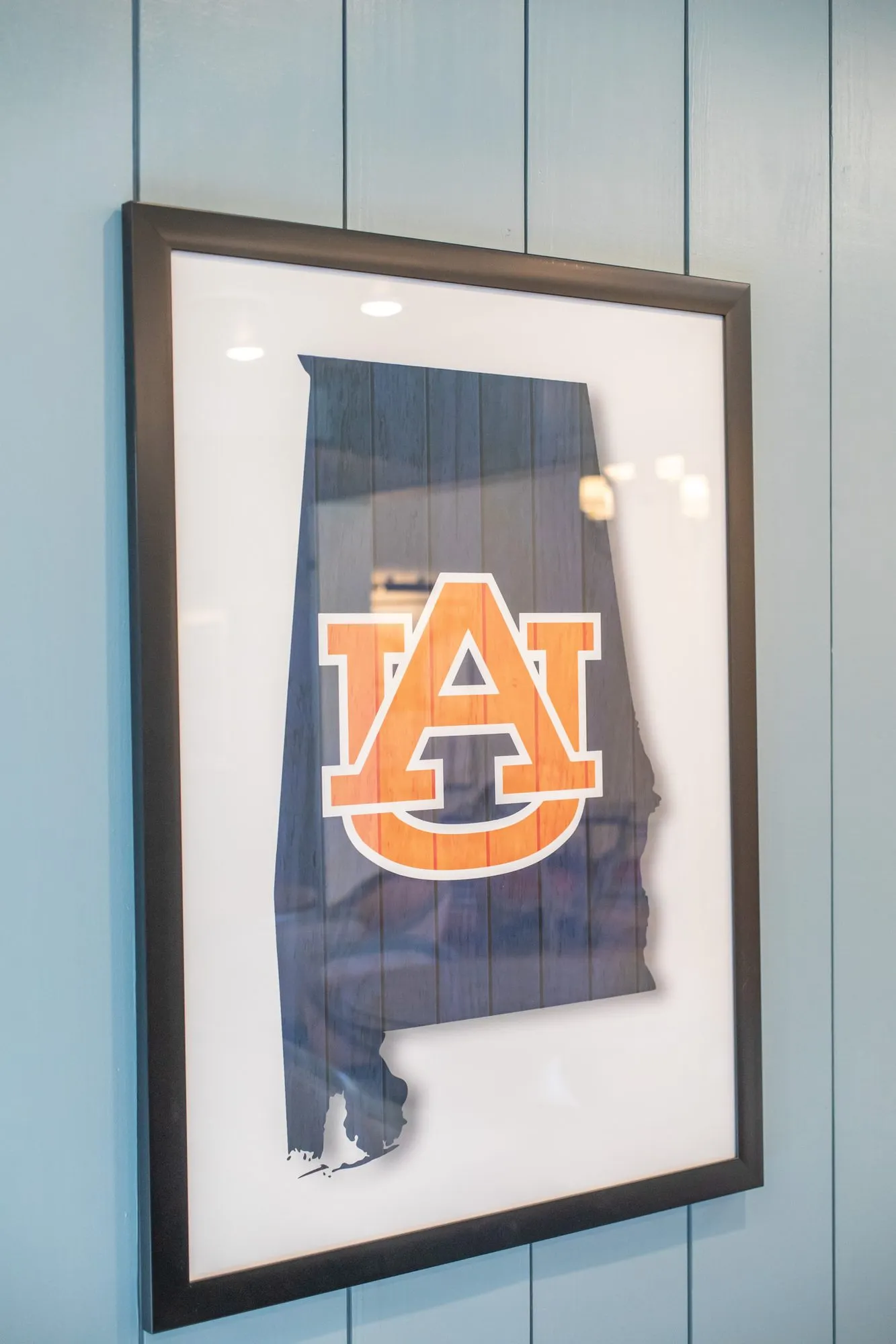 Senior living interior detail: framed Alabama state outline with an orange university monogram on blue shiplap
