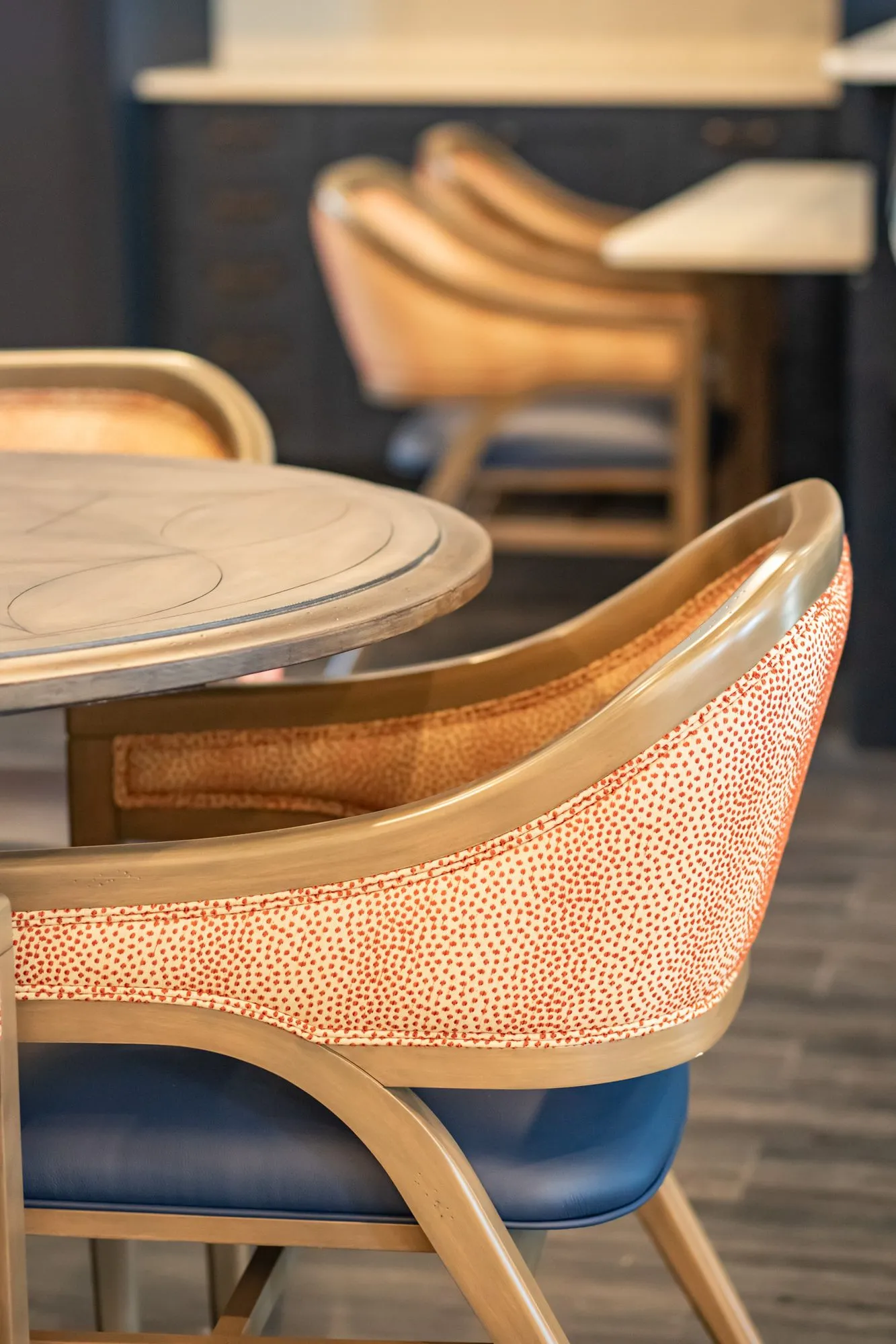 Senior living interior detail: coral dot chair with a blue seat at a round table, barstools beyond