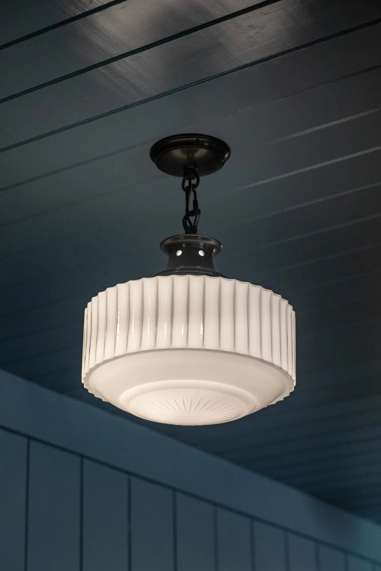 Senior living interior detail: ribbed white glass pendant on a black chain under a navy plank ceiling