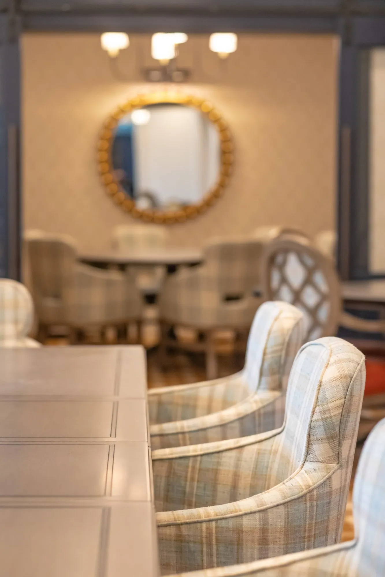 Senior living private dining room, along a long table with plaid chairs toward a gilt beaded mirror