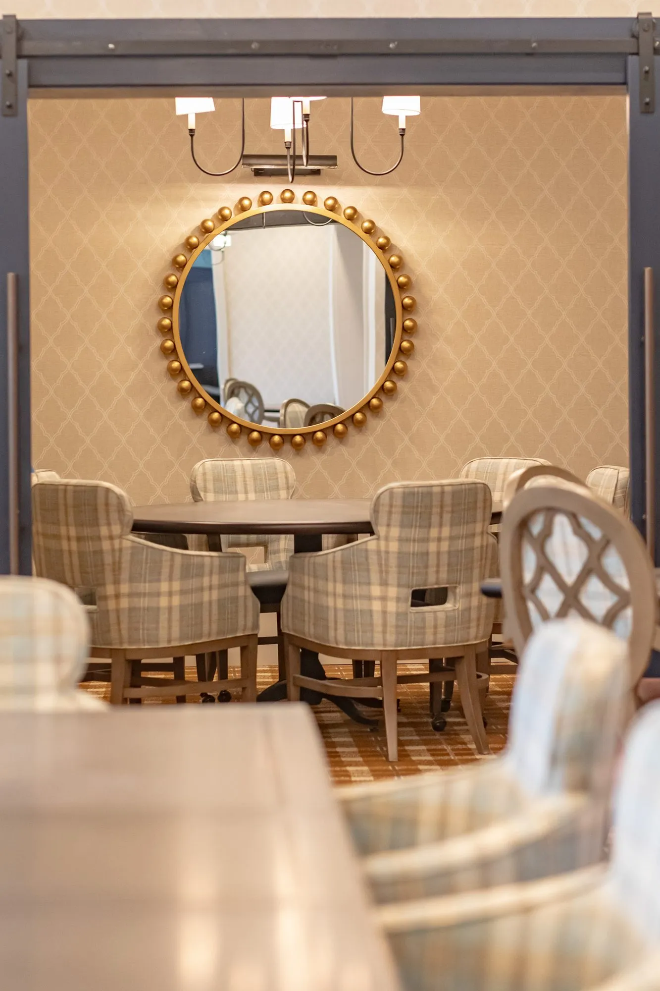 Senior living private dining room seen through barn doors, plaid chairs below a gilt beaded mirror