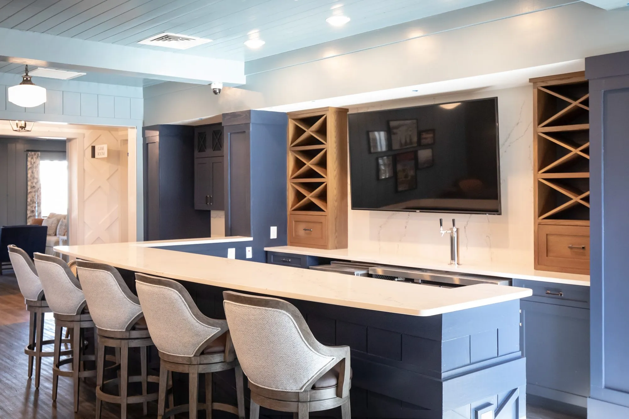 Senior living bar with herringbone swivel stools at a navy counter, wine racks and a TV on the back wall
