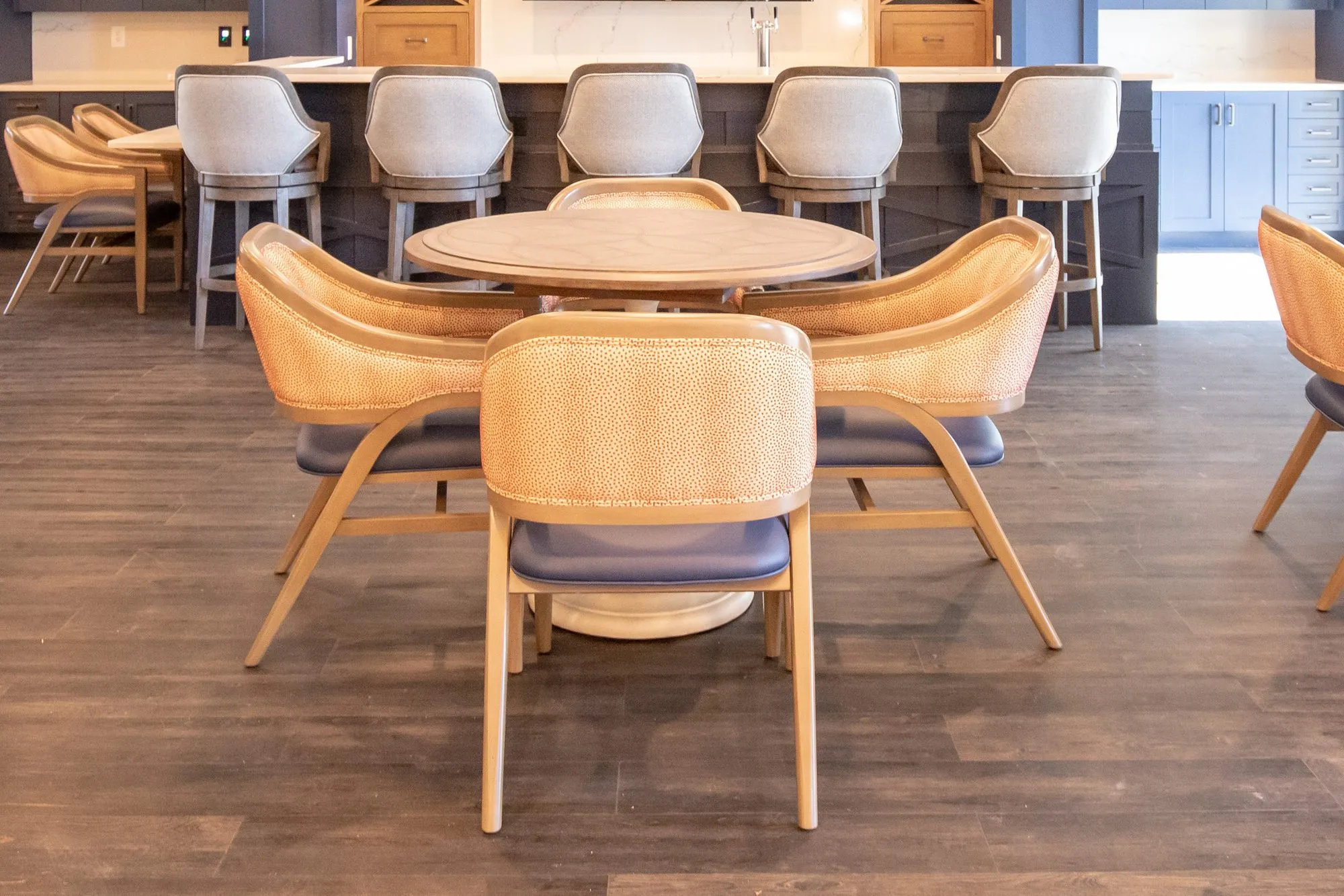 Senior living pub with coral dot chairs around a round table before a row of grey barstools at the bar