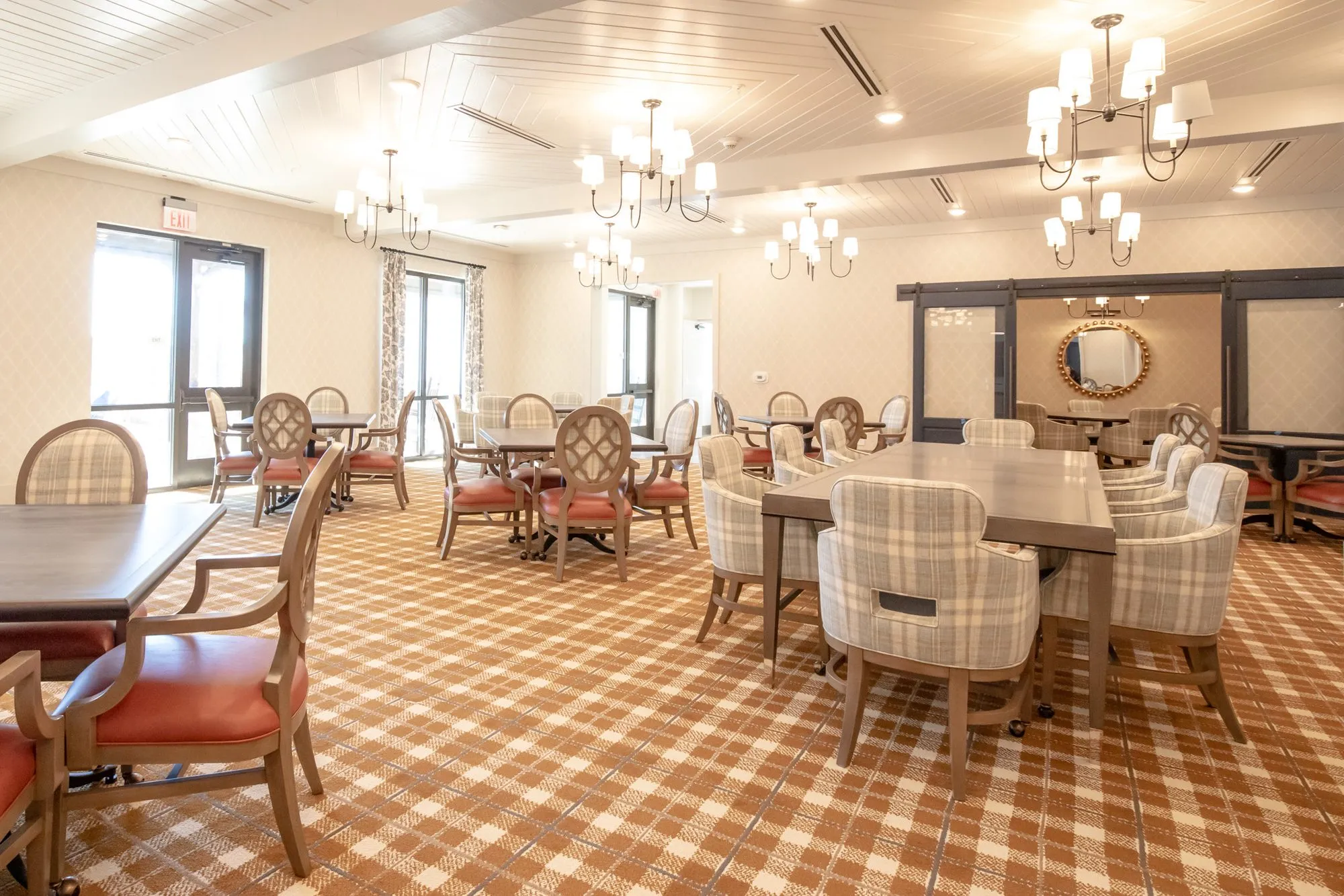 Senior living dining room with plaid chairs at long tables and quatrefoil chairs under candle chandeliers