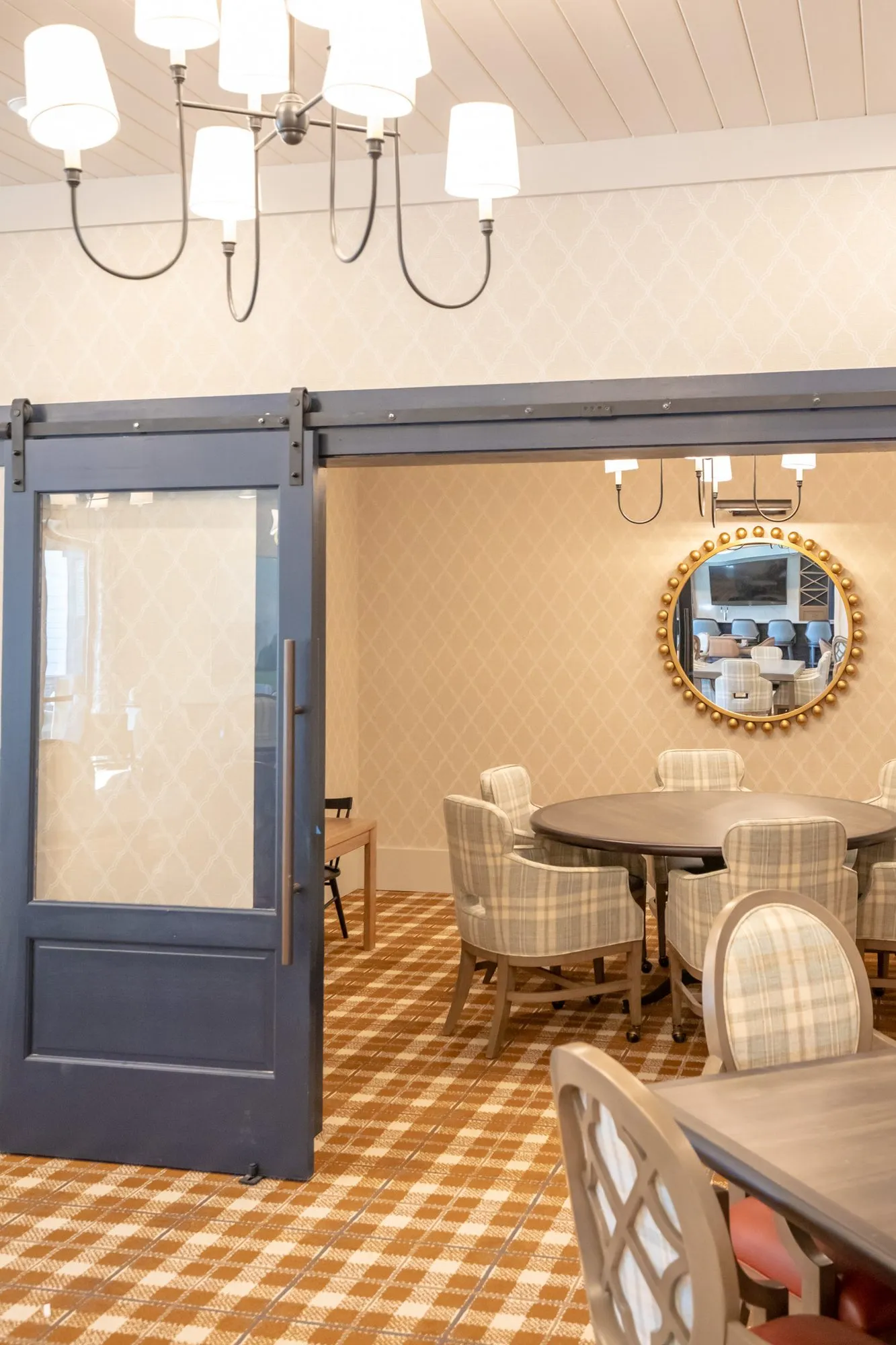 Senior living private dining room past a navy barn door, a gilt beaded mirror on the wall