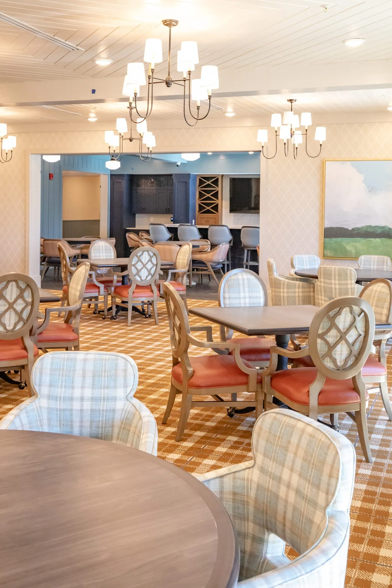 Senior living dining room with coral seated quatrefoil chairs at square tables toward the bar