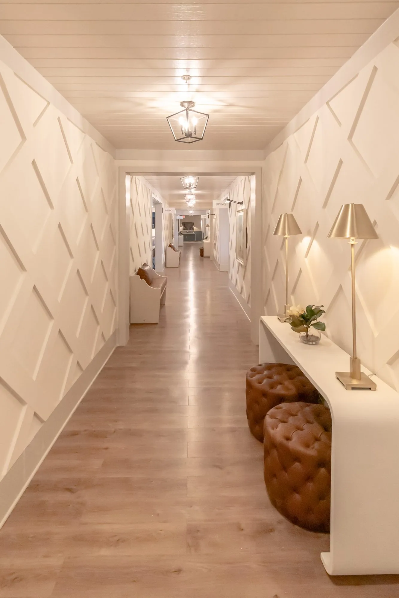 Senior living corridor with diamond panelling, brass lamps on a white console and leather ottomans