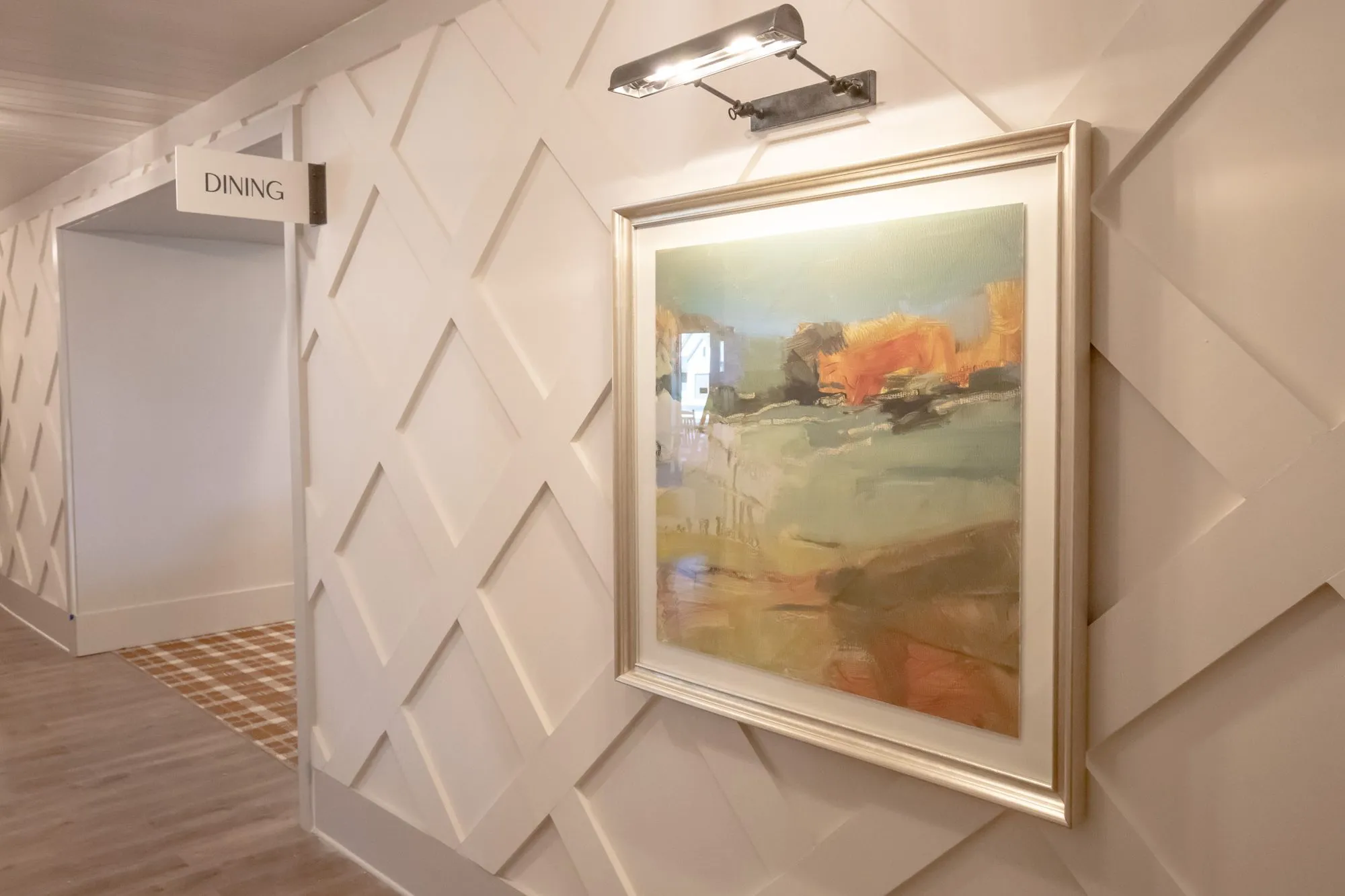 Senior living interior detail: abstract landscape with a picture light on diamond panelled millwork beside a Dining sign