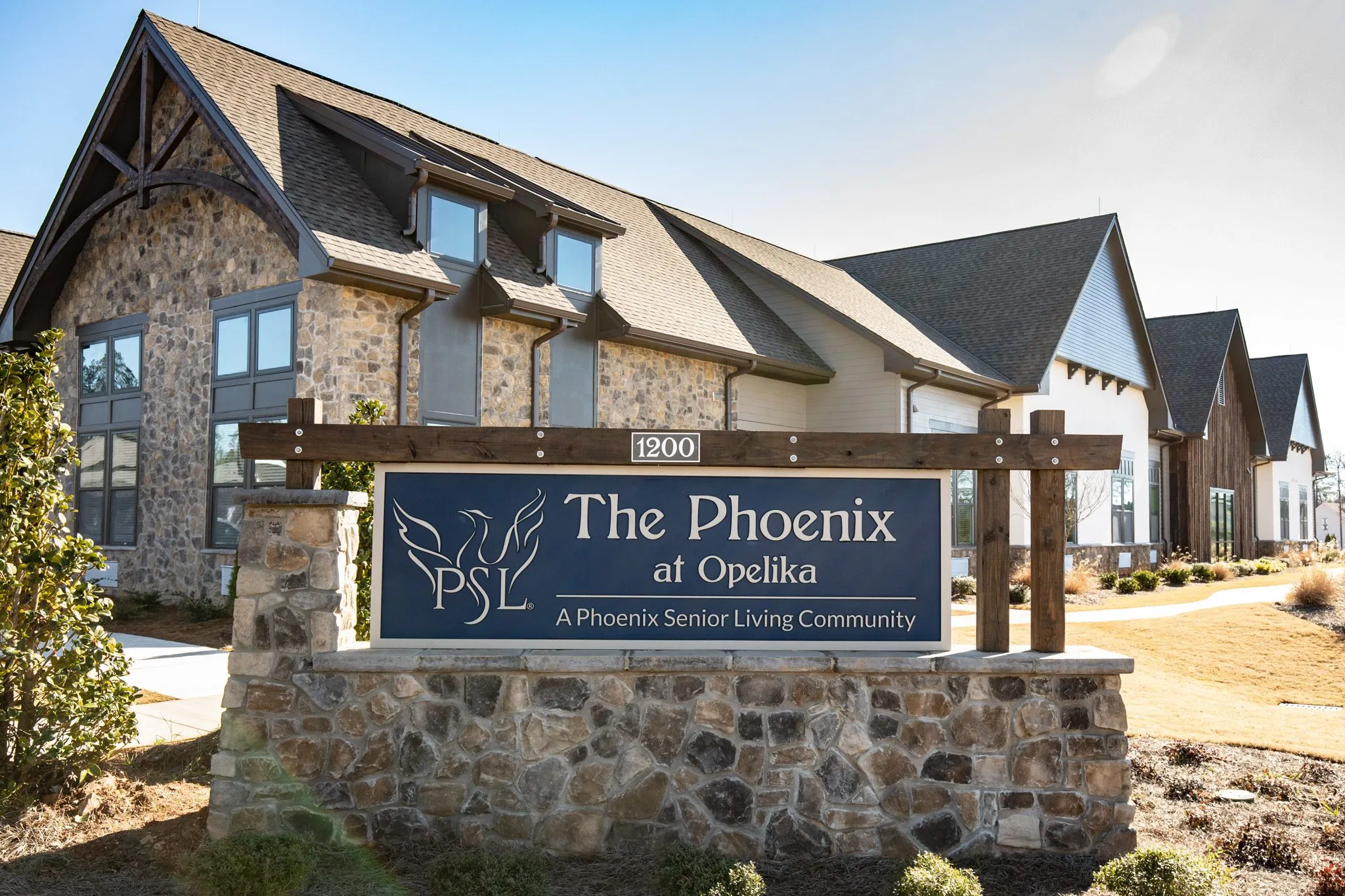 Senior living community entrance with the stone monument sign before the gabled stone and shingle building