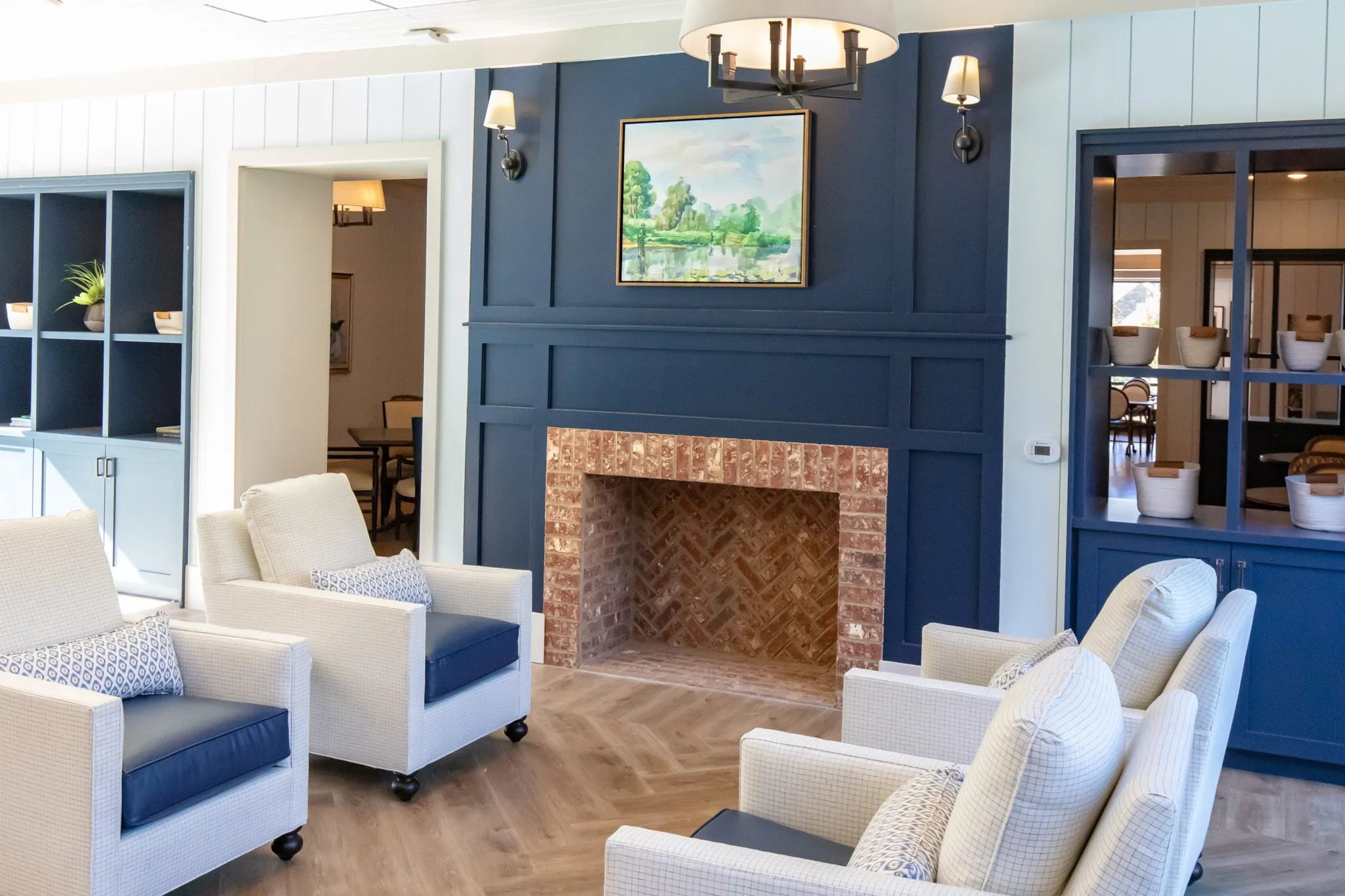 Senior living lounge with a herringbone brick firebox set into a navy panelled wall, cream and navy chairs